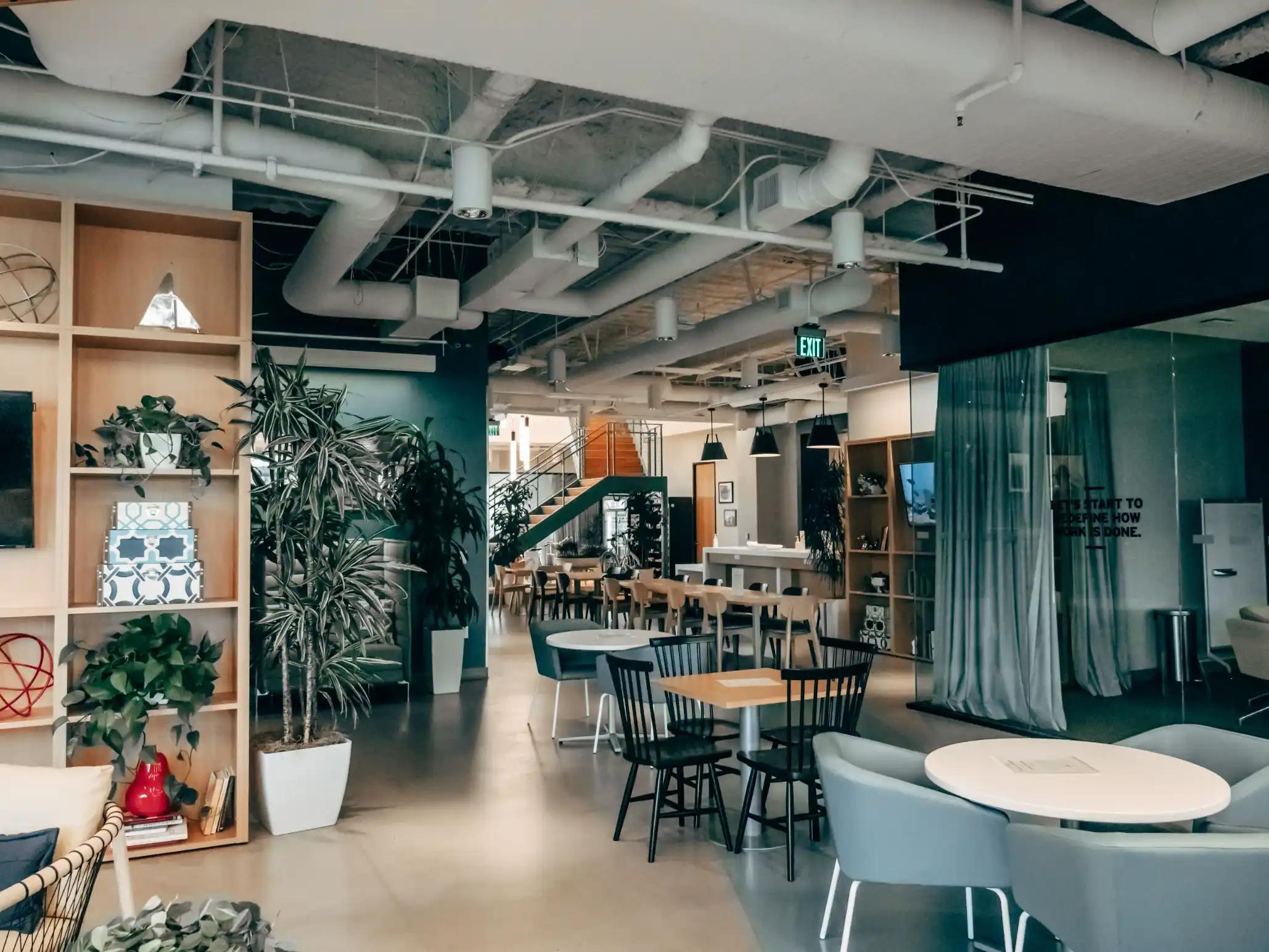 Bright open-plan office with cafe-style tables and a shared kitchen area where staff gather for lunch