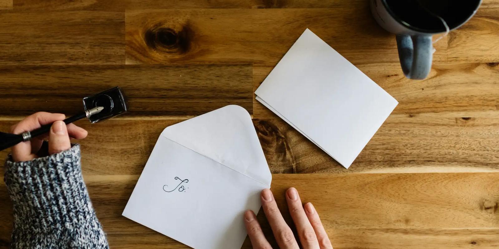 Iemand schrijft een persoonlijke kaart met envelop op een houten tafel