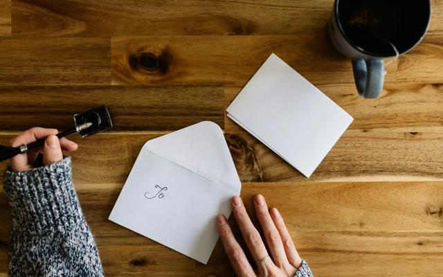 Iemand schrijft een persoonlijke kaart met envelop op een houten tafel