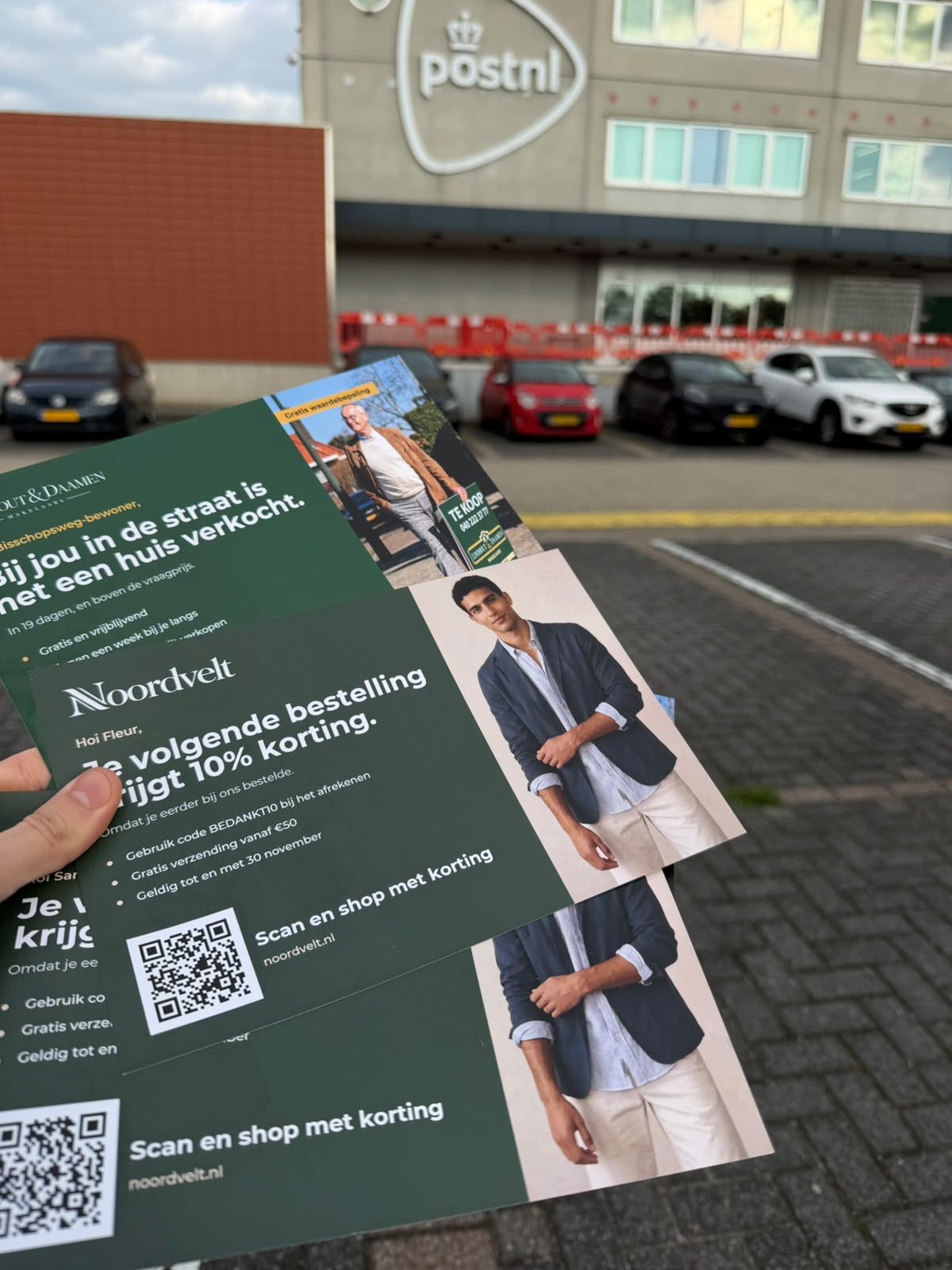 Hand holding a batch of printed postcards with QR codes outside a postal distribution centre