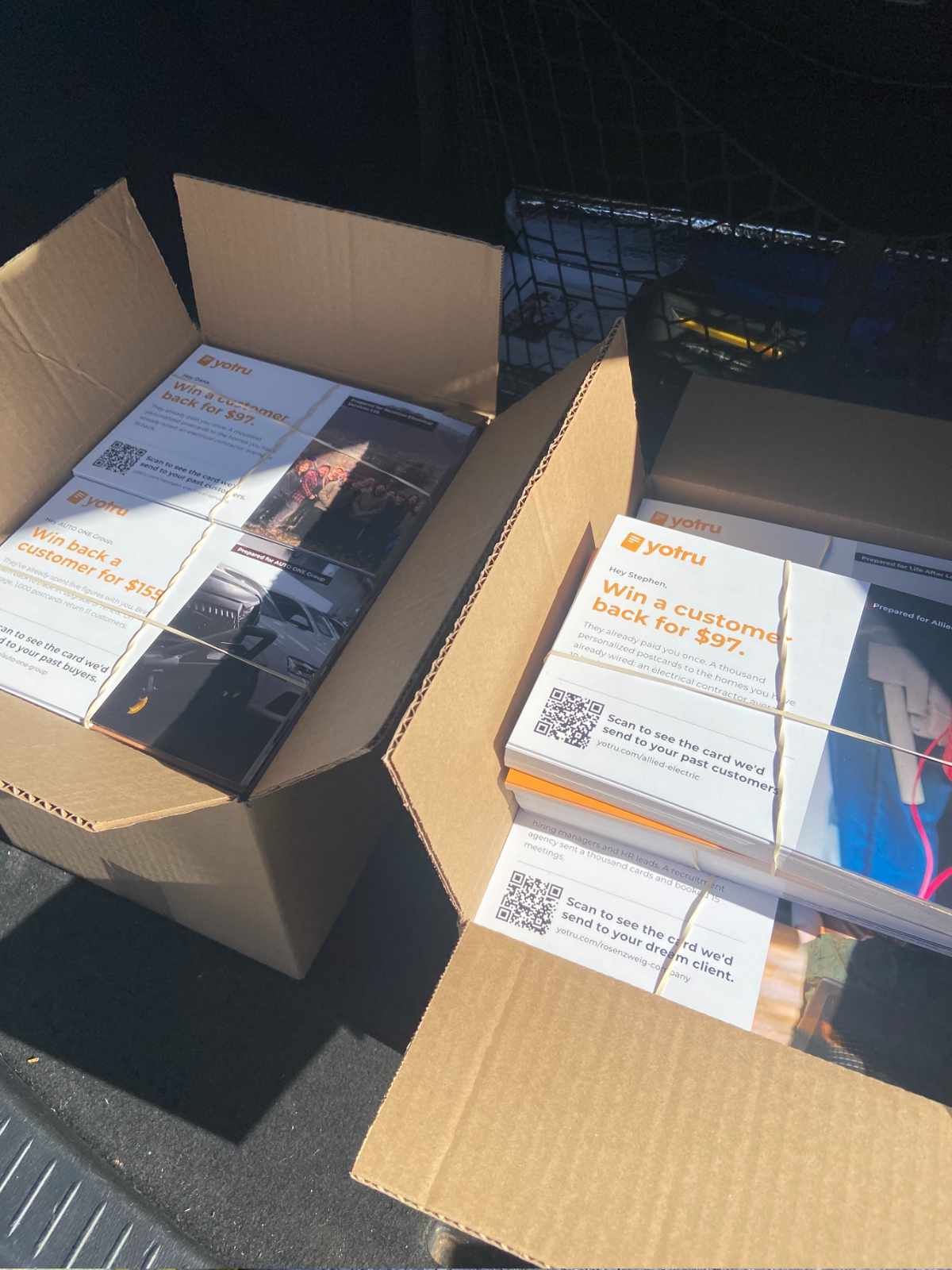 Two open boxes of printed Yotru postcards, each with its own QR code, bundled and ready for mailing