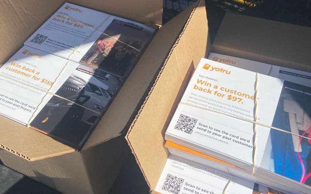 Two open boxes of printed Yotru postcards, each with its own QR code, bundled and ready for mailing