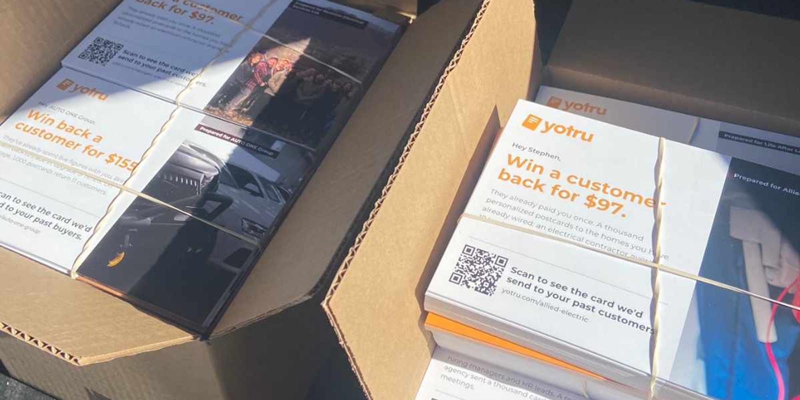 Two open boxes of printed Yotru postcards, each with its own QR code, bundled and ready for mailing