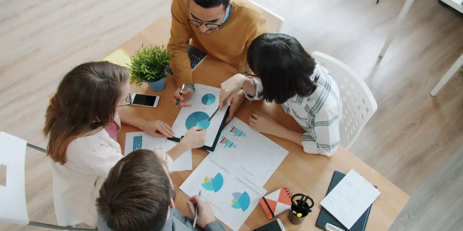 Overhead view of a team around a table reviewing campaign charts and printed reports