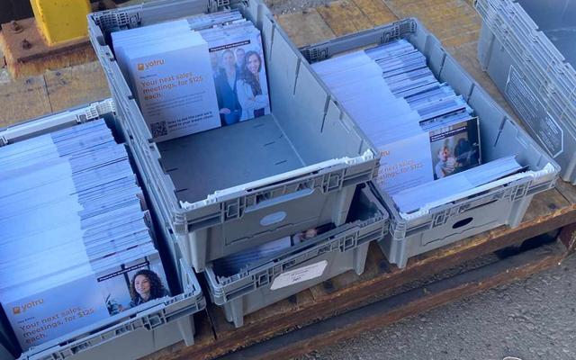 Postal trays filled with sorted, addressed postcards ready for drop-off at a mail facility