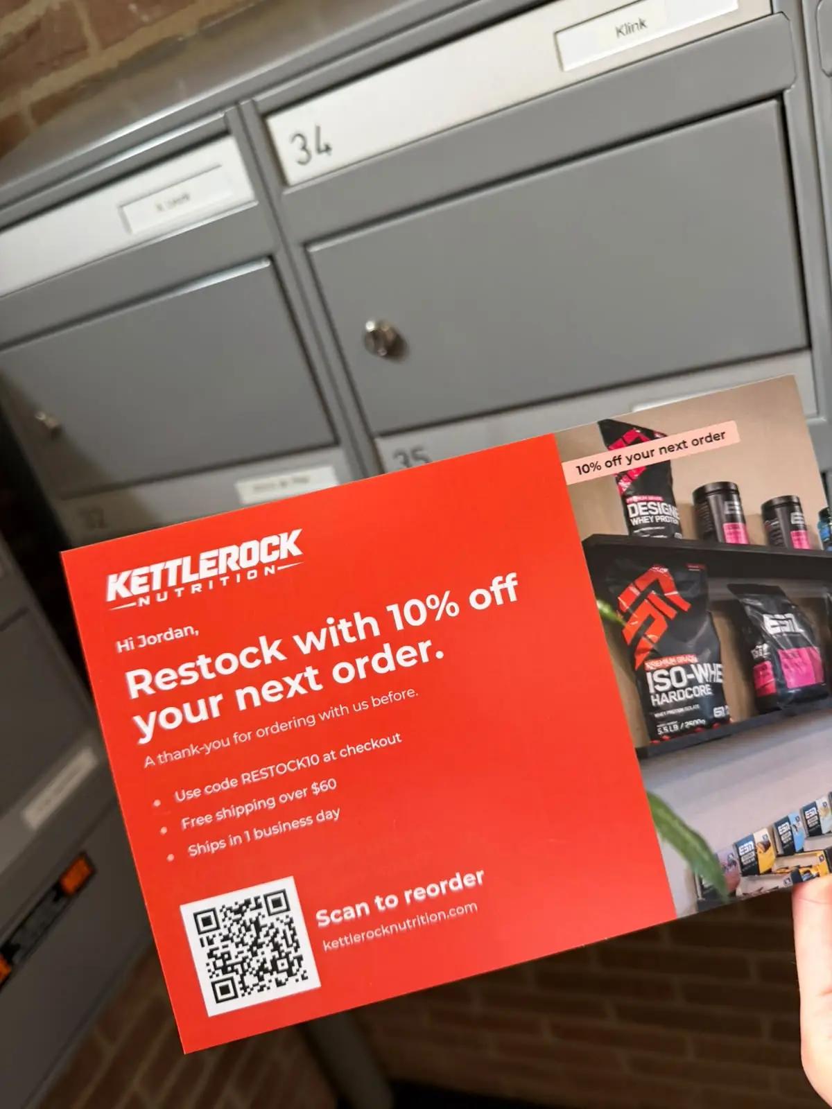 Hand holding a red reactivation postcard offering 10% off a returning customer's next order, with a QR code to reorder, in front of mailboxes