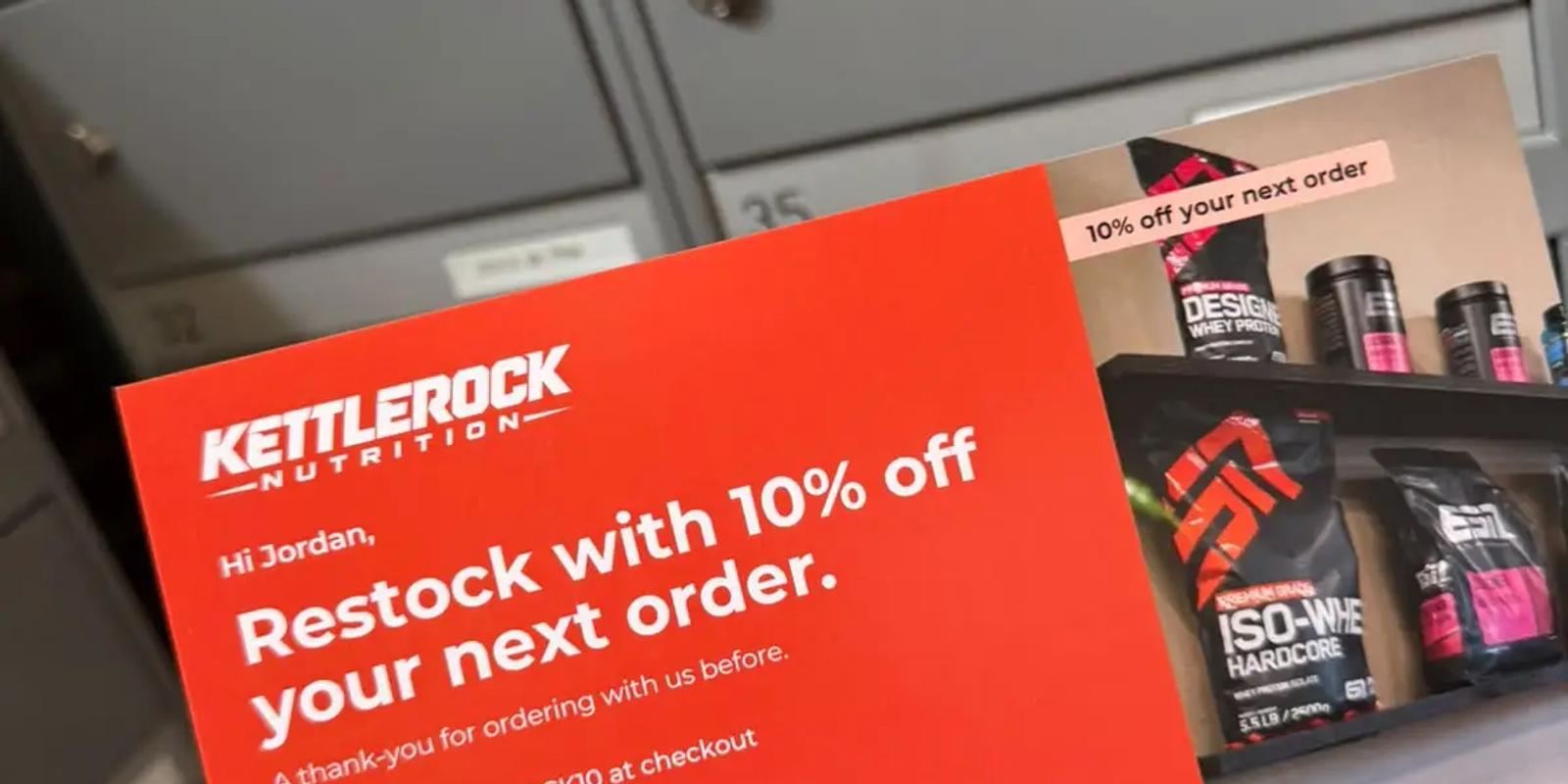 Hand holding a red reactivation postcard offering 10% off a returning customer's next order, with a QR code to reorder, in front of mailboxes