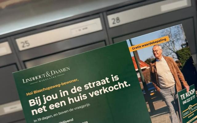 Hand houdt een persoonlijke kaart met QR-code vast voor een rij brievenbussen in een bakstenen portiek