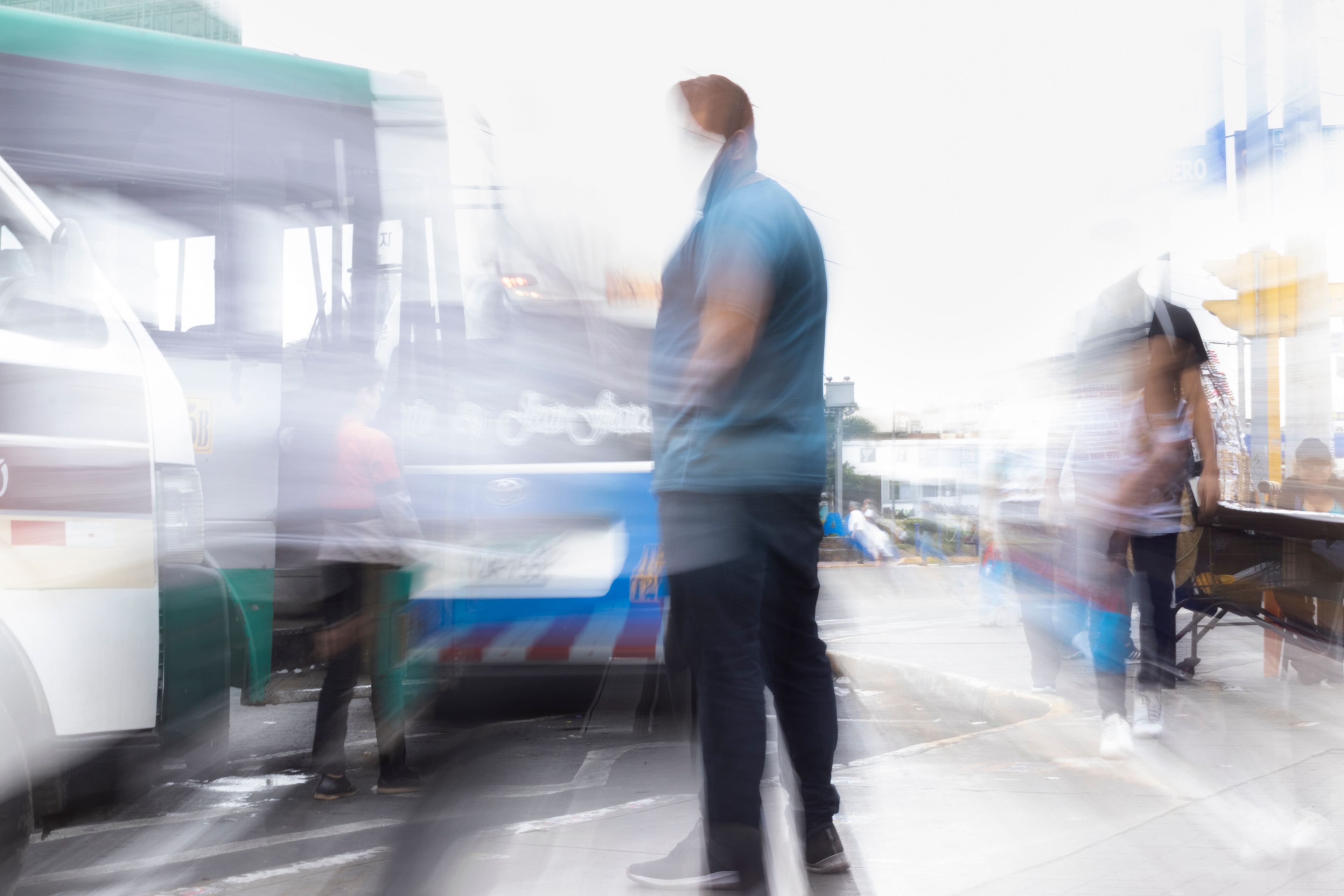 Hombre de pie en una zona de transporte donde las personas y los vehículos se ven en movimiento borroso