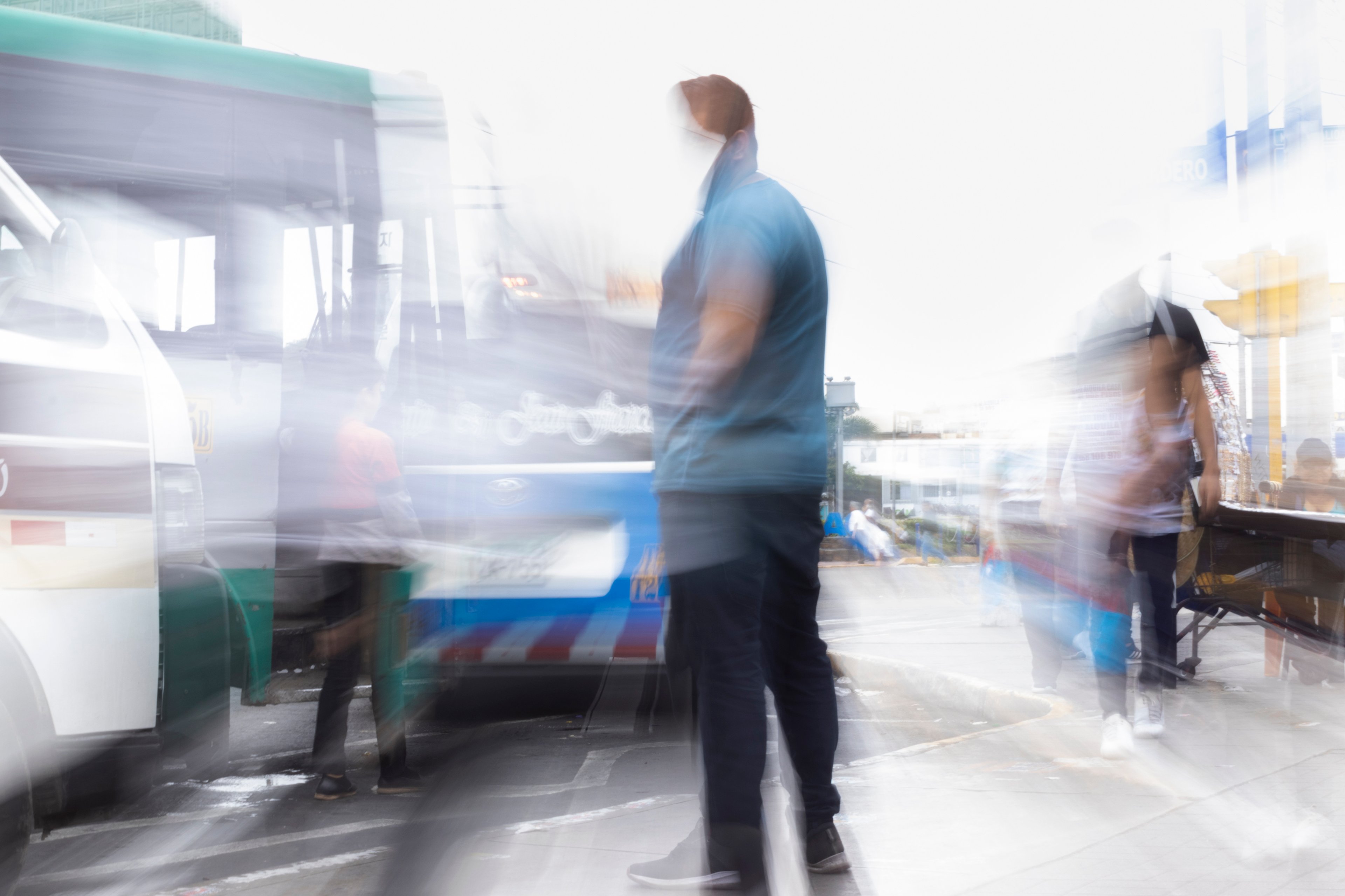 Hombre de pie en una zona de transporte donde las personas y los vehículos se ven en movimiento borroso