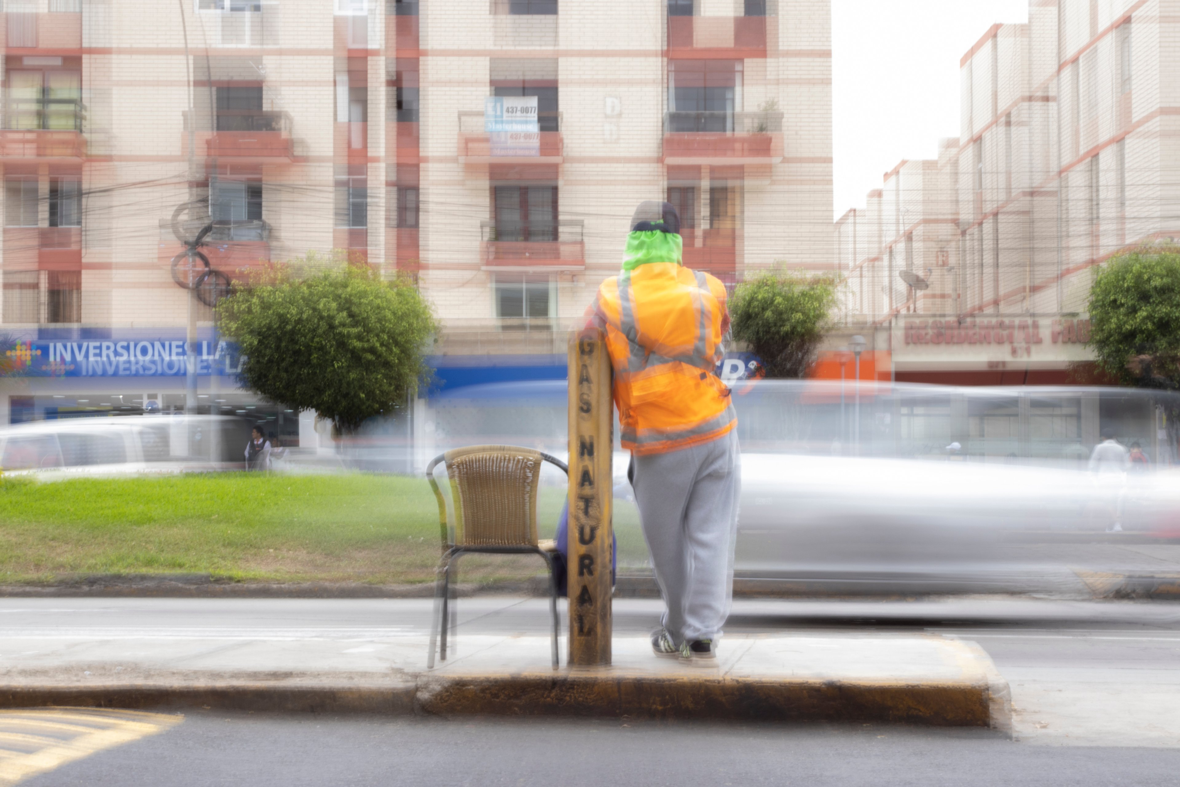 Persona con chaleco naranja apoyada en un poste mientras los autos pasan borrosos a su alrededor