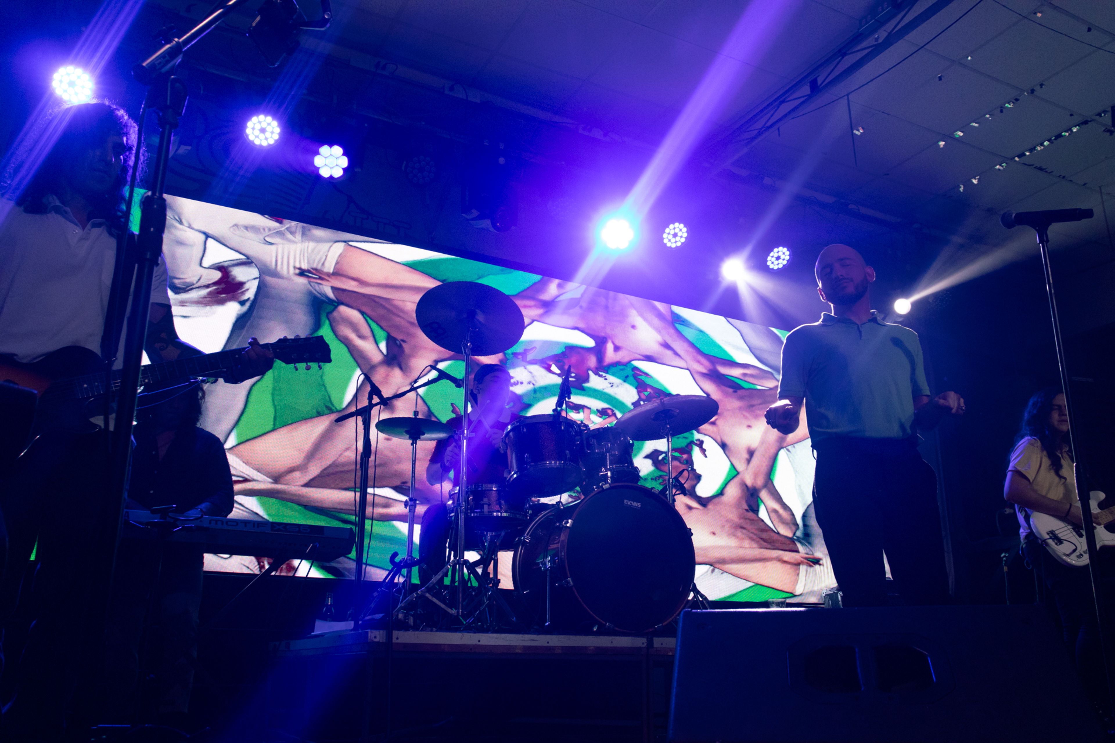 Banda tocando en un escenario con una gran pantalla iluminada detrás, mostrando visuales coloridos