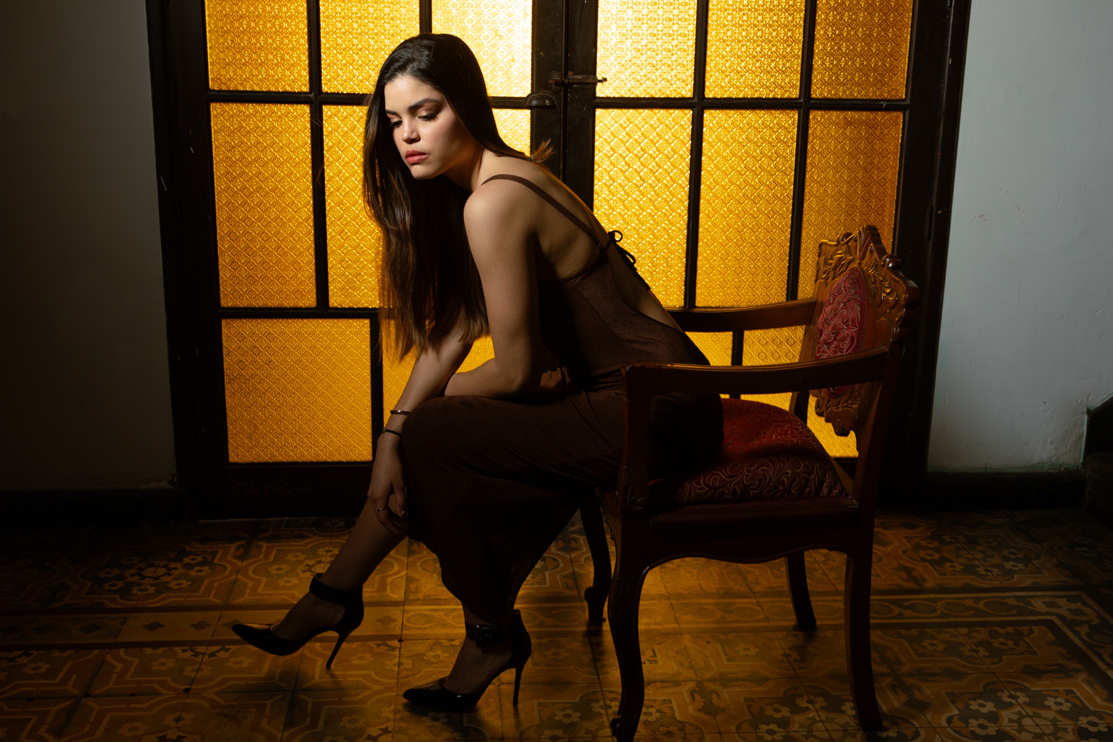 Retrato editorial de una modelo sentada frente a una ventana iluminada en tonos cálidos