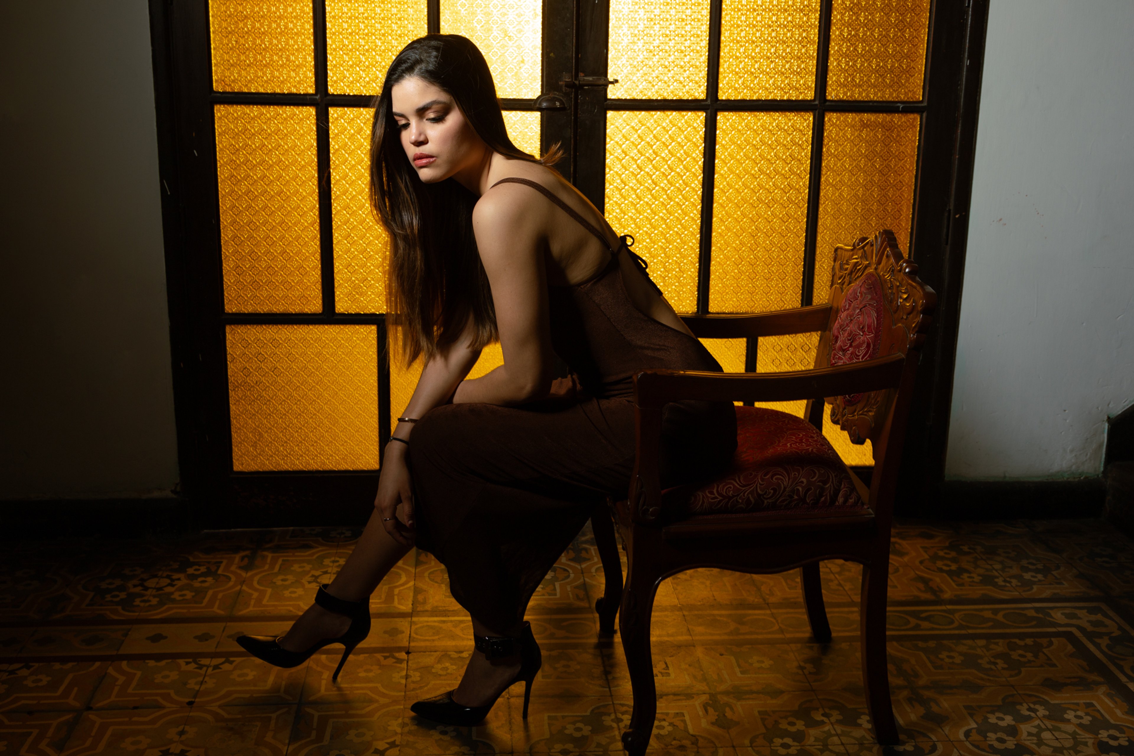 Retrato editorial de una modelo sentada frente a una ventana iluminada en tonos cálidos