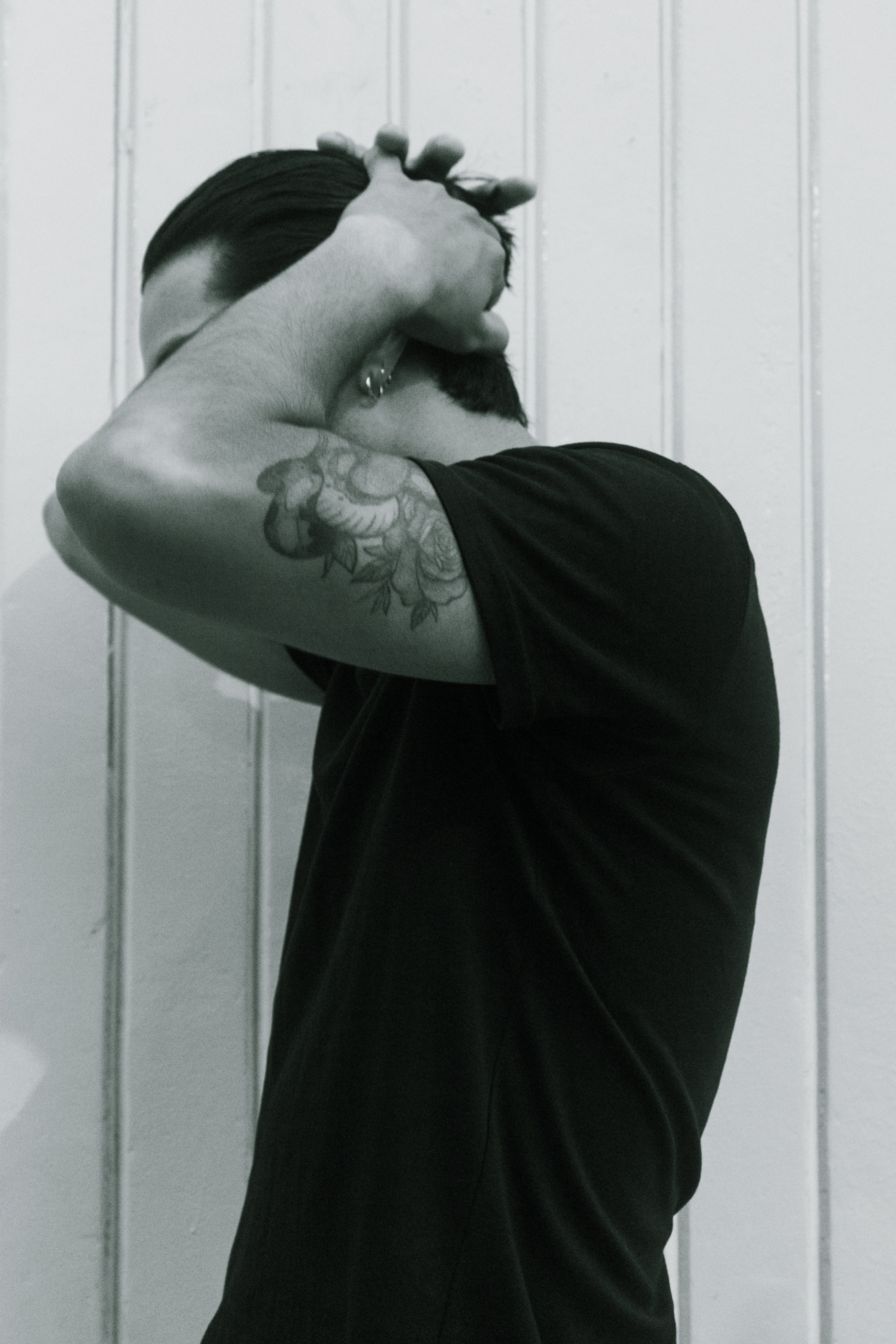 Retrato en interiores de un joven ajustándose el cabello, con tatuaje visible en el brazo