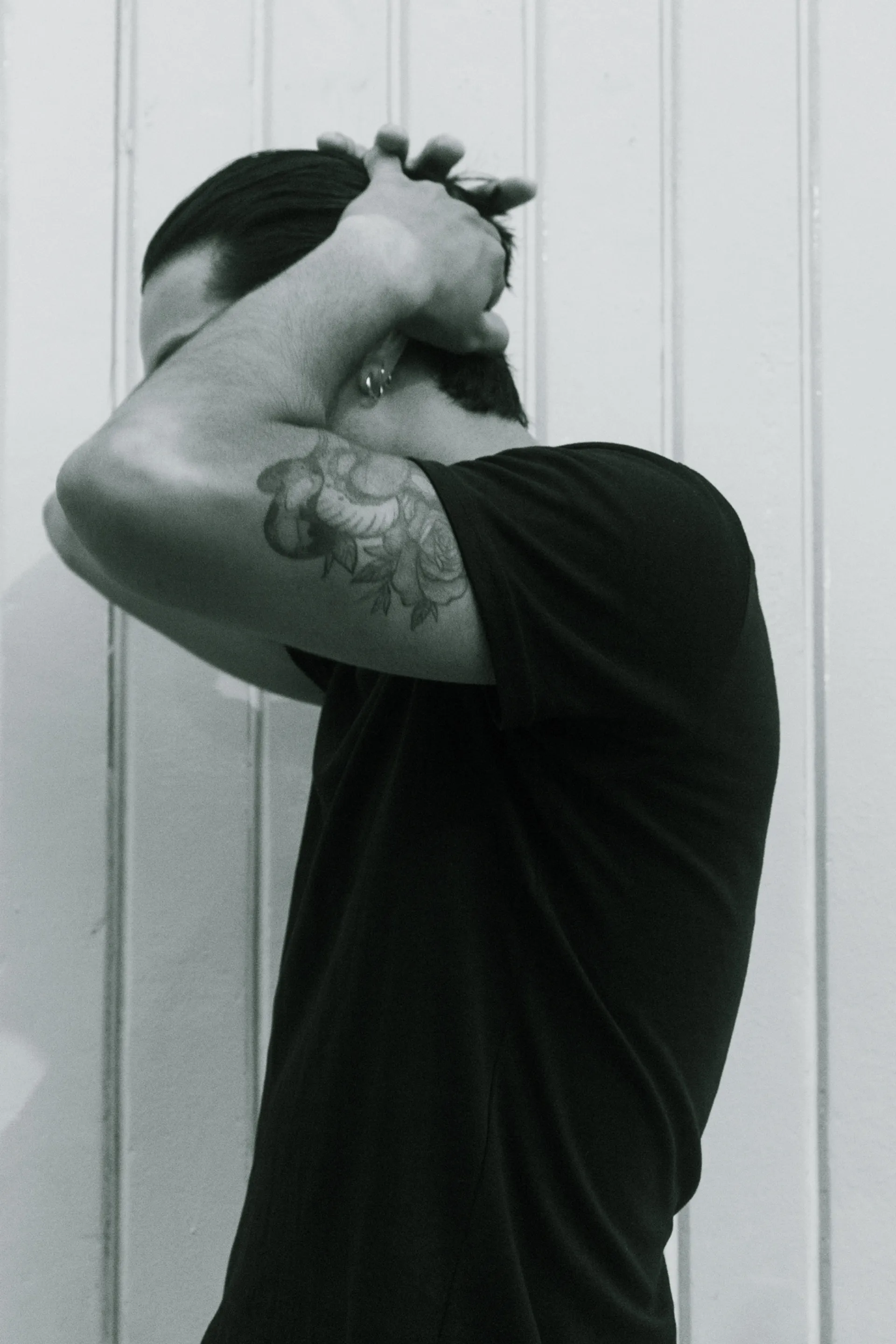 Retrato en interiores de un joven ajustándose el cabello, con tatuaje visible en el brazo