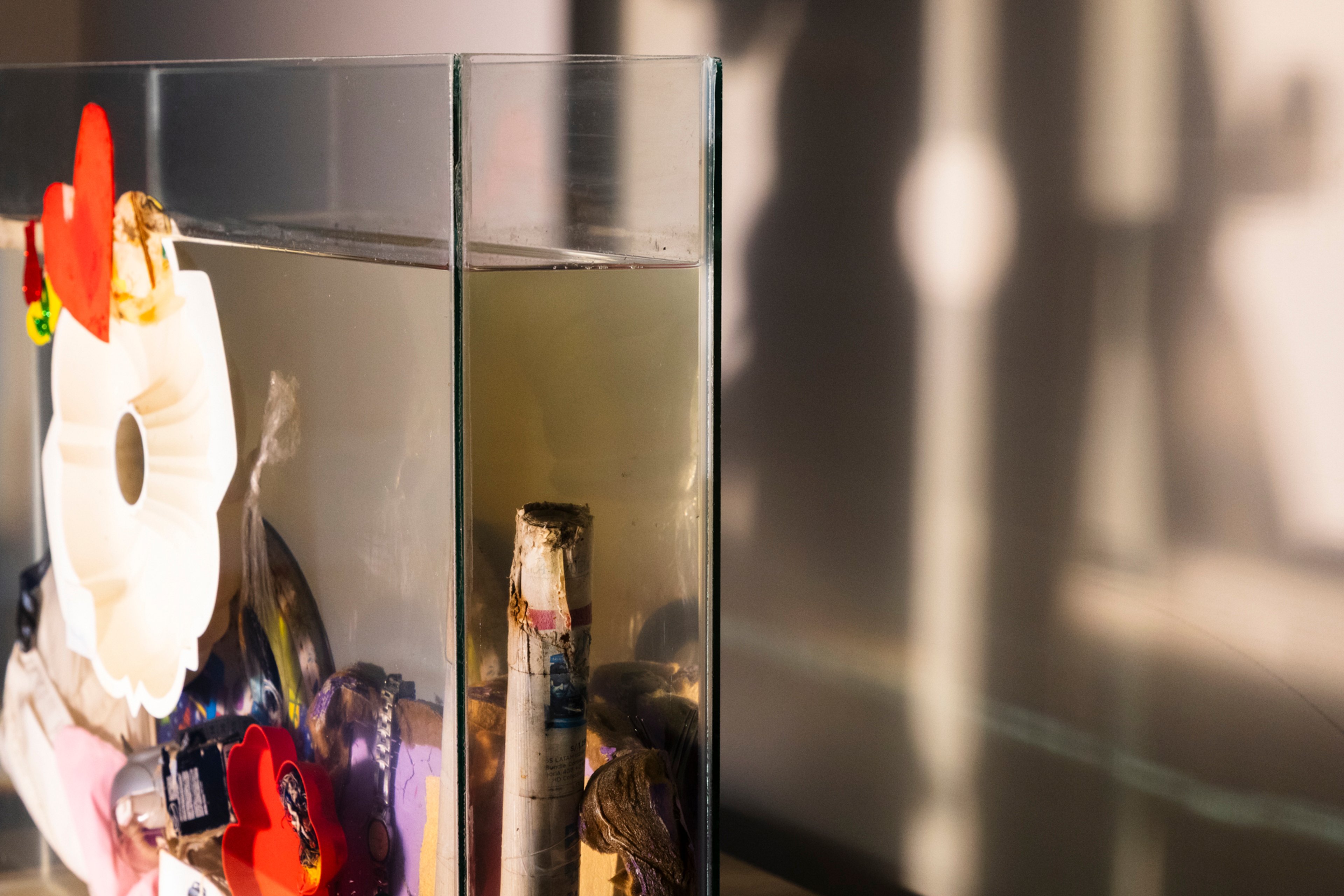 Objetos personales sumergidos en agua turbia dentro de una pecera de vidrio.