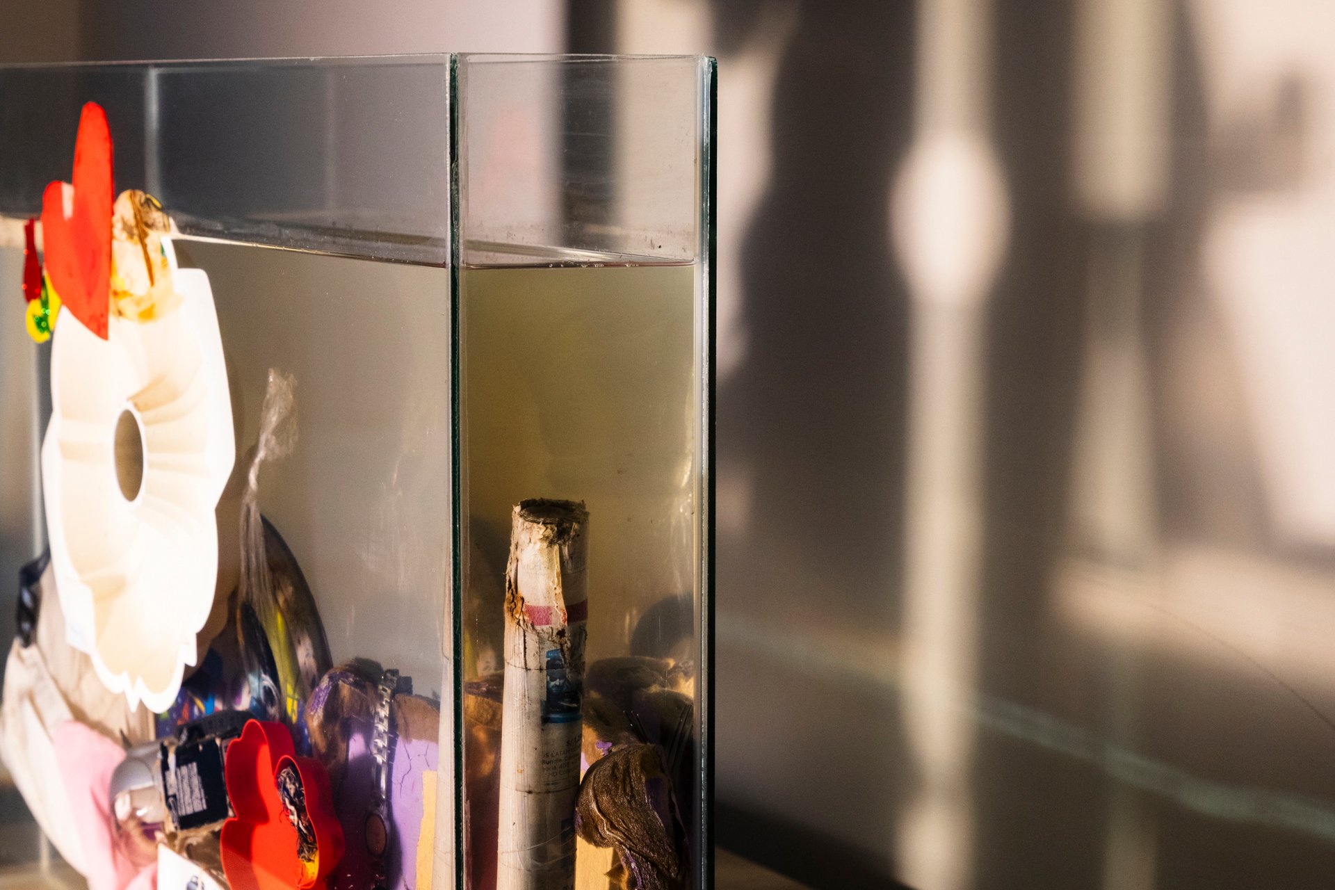 Objetos personales sumergidos en agua turbia dentro de una pecera de vidrio.