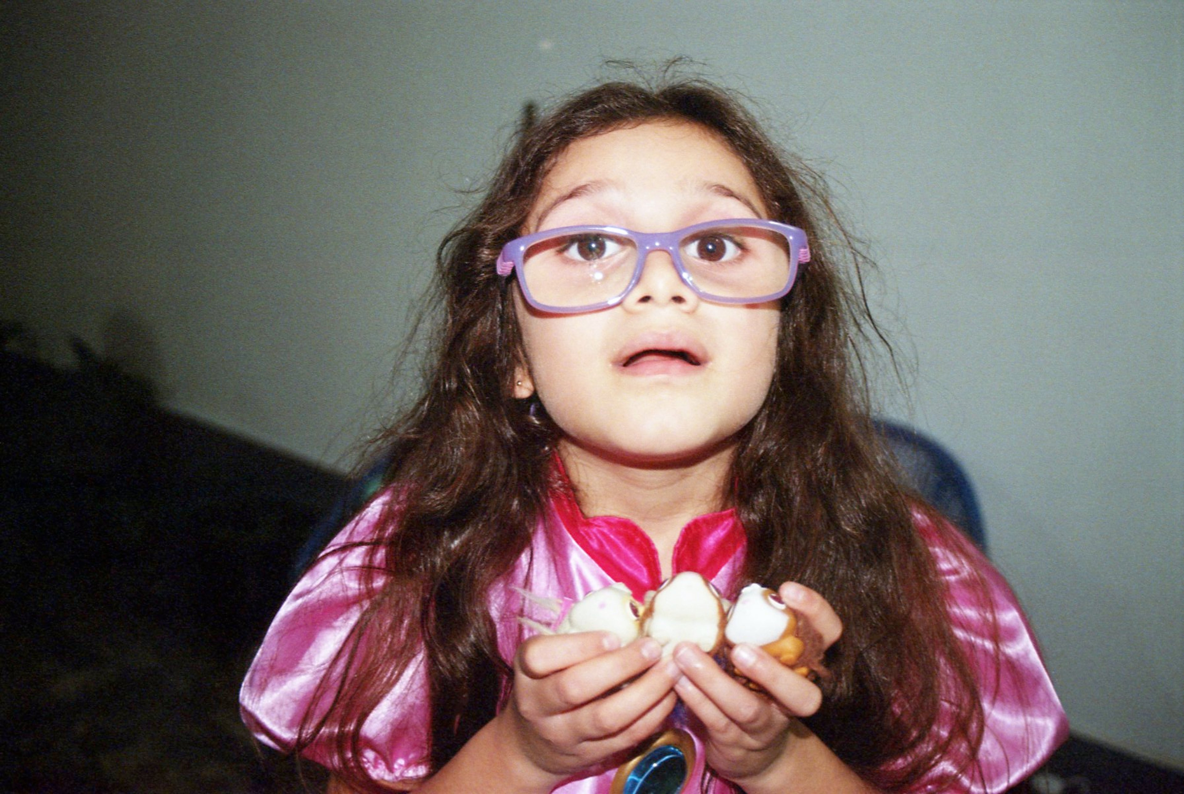 Niña con lentes grandes y vestido rosado sosteniendo varios bocaditos en una fiesta