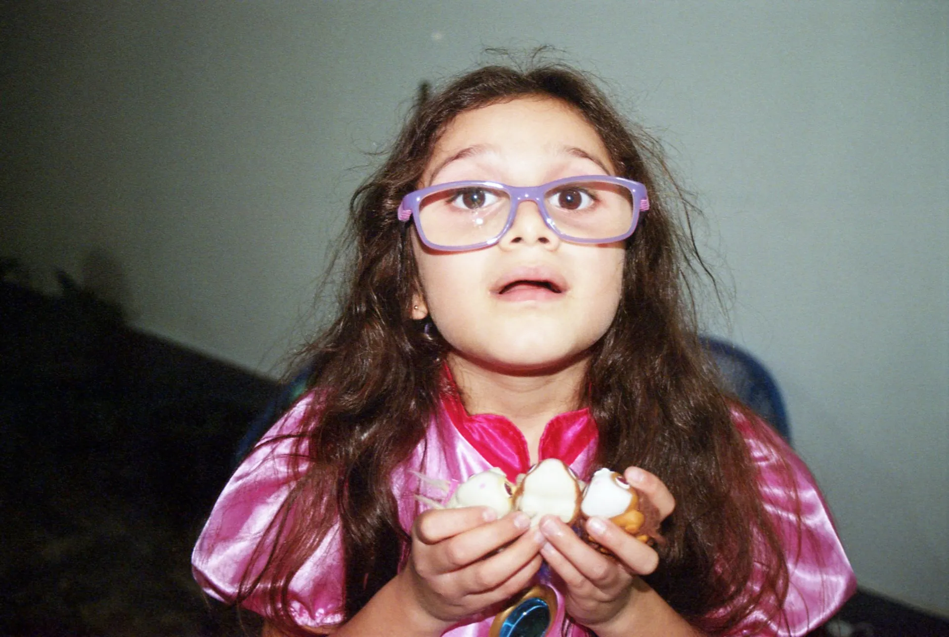 Niña con lentes grandes y vestido rosado sosteniendo varios bocaditos en una fiesta