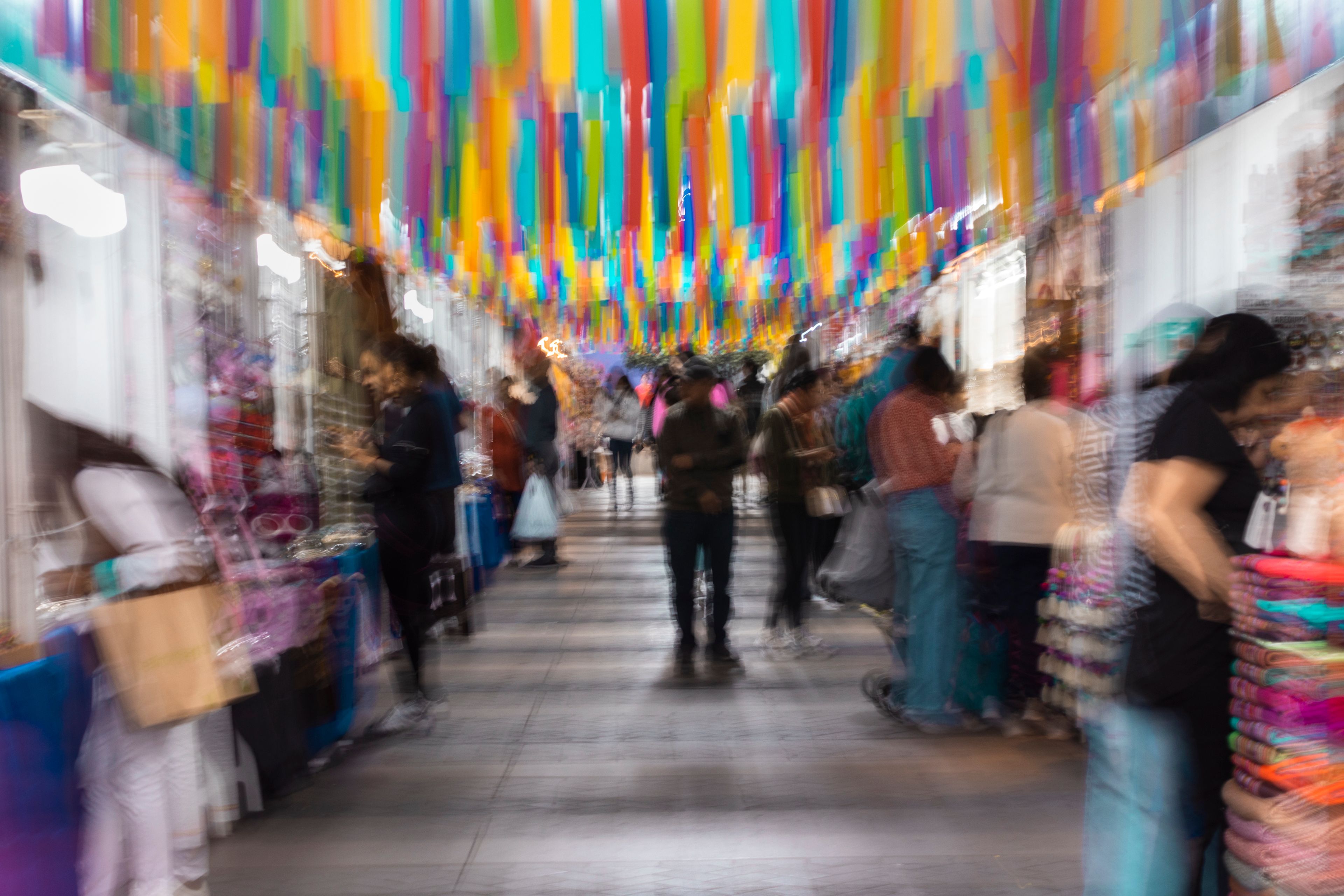 Pasillo de mercado con personas difuminadas y cintas de colores vibrantes en el techo