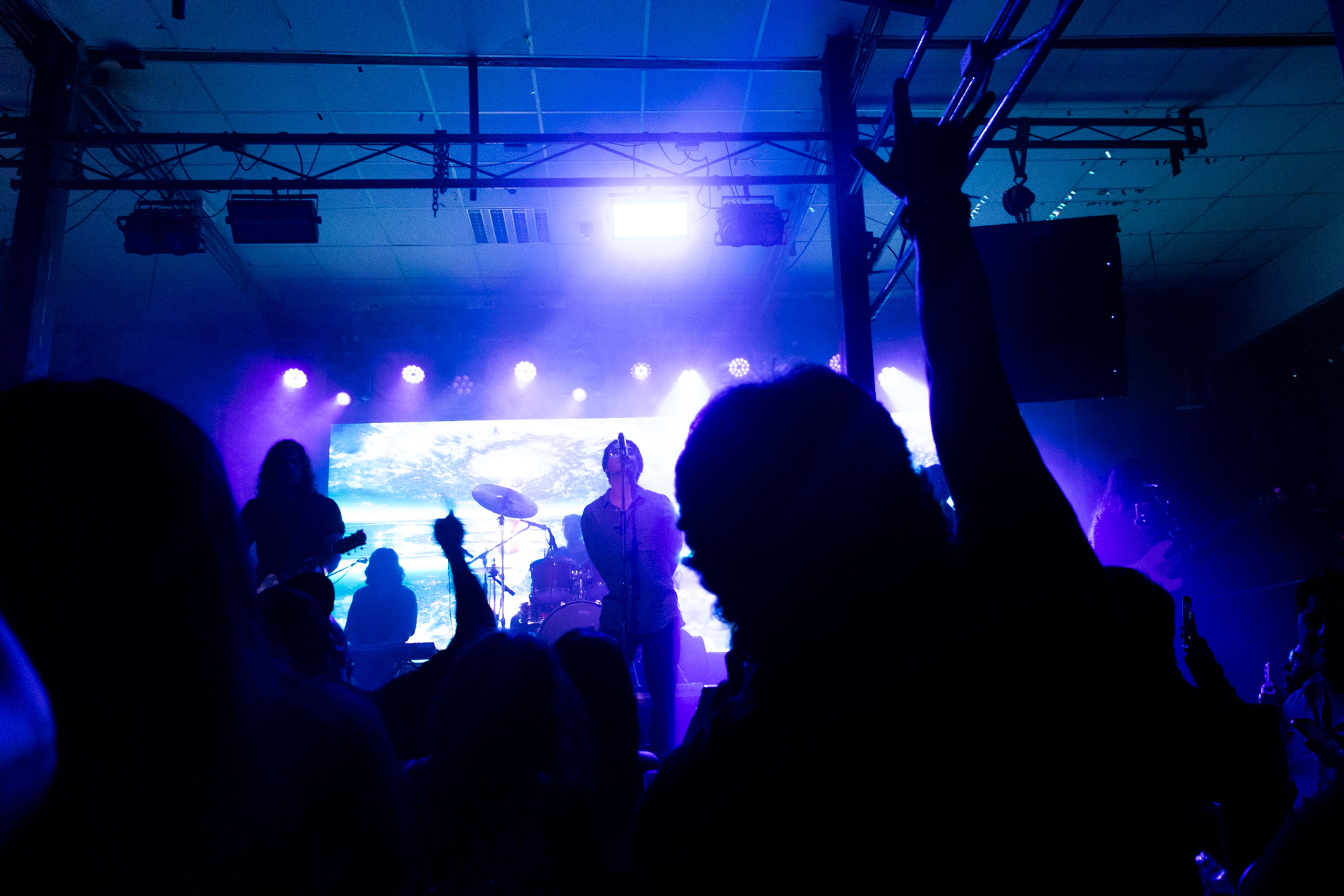 Público levantando la mano frente a una banda tocando en un escenario con luces azules