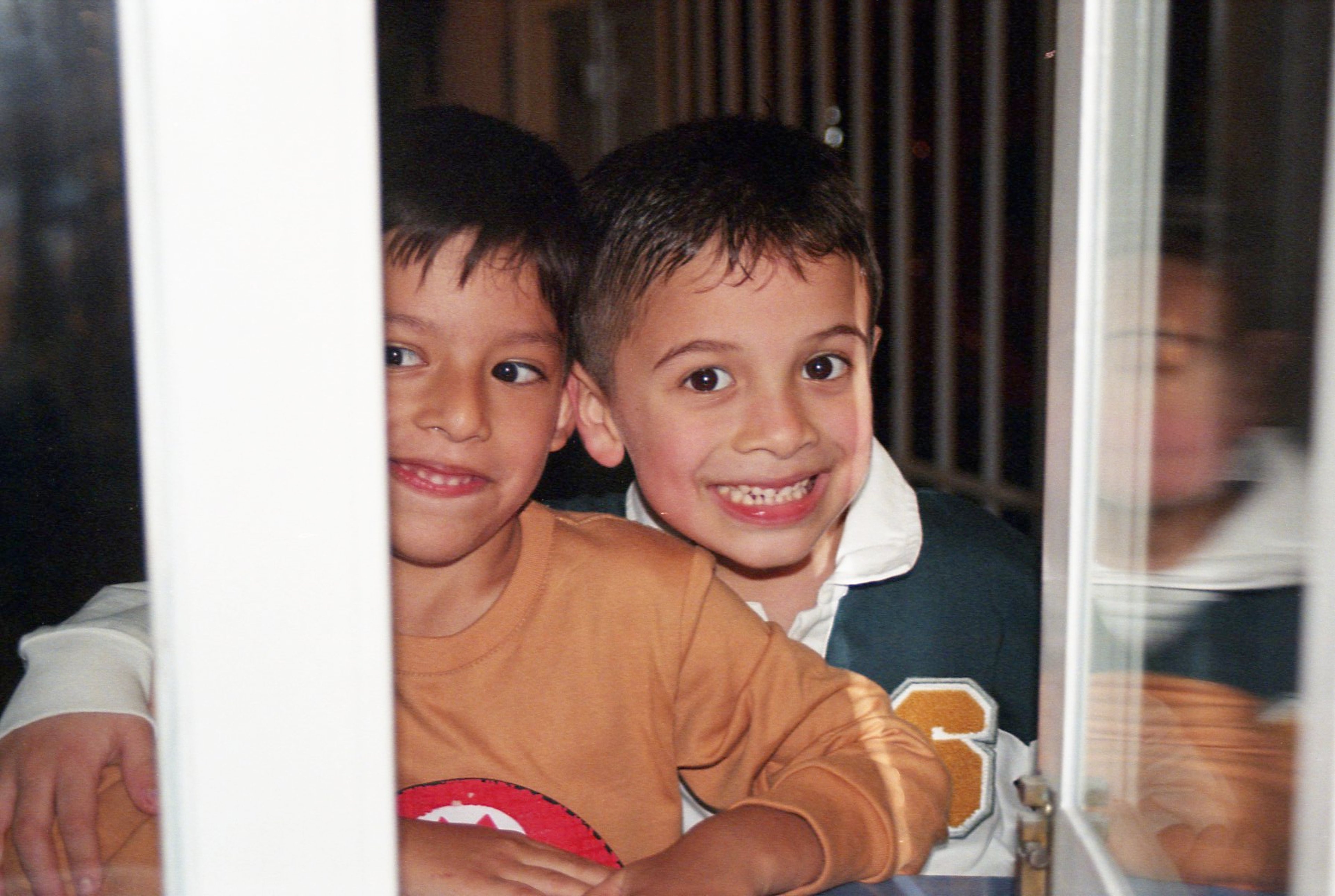 Dos niños asomándose por una ventana con expresiones alegres