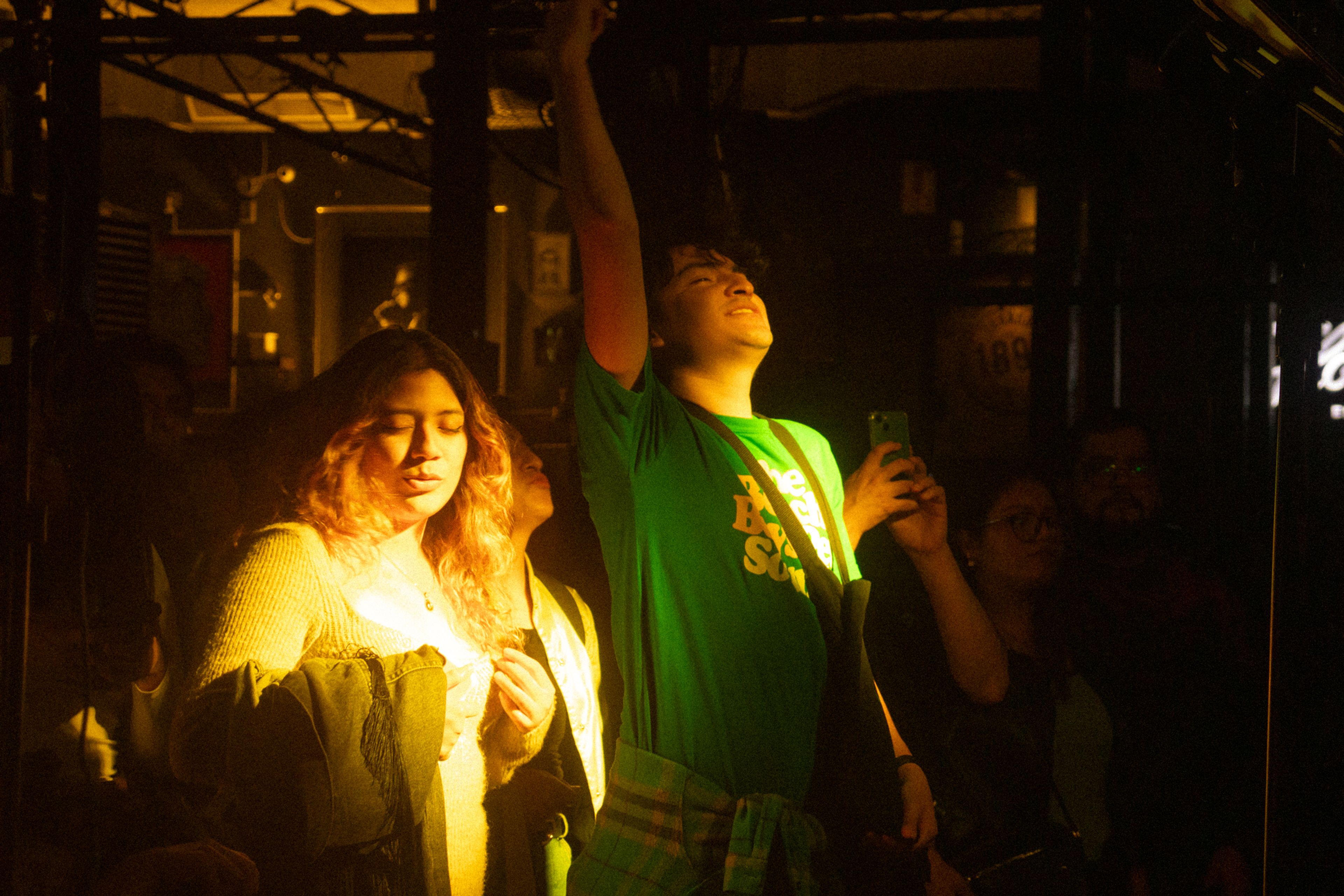 Joven levantando el brazo bajo una luz amarilla intensa durante un concierto