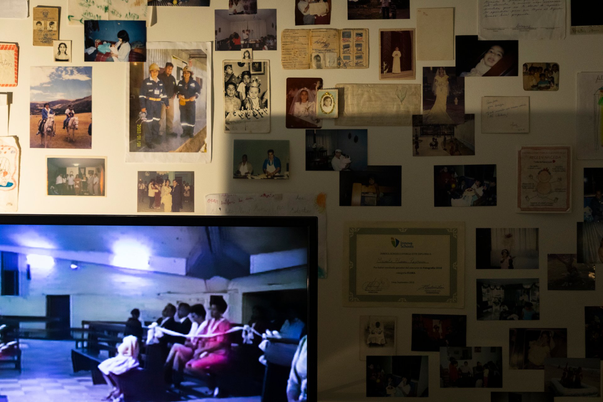 Detalle del mural de fotografías y documentos, con la pantalla del televisor encendida en primer plano.