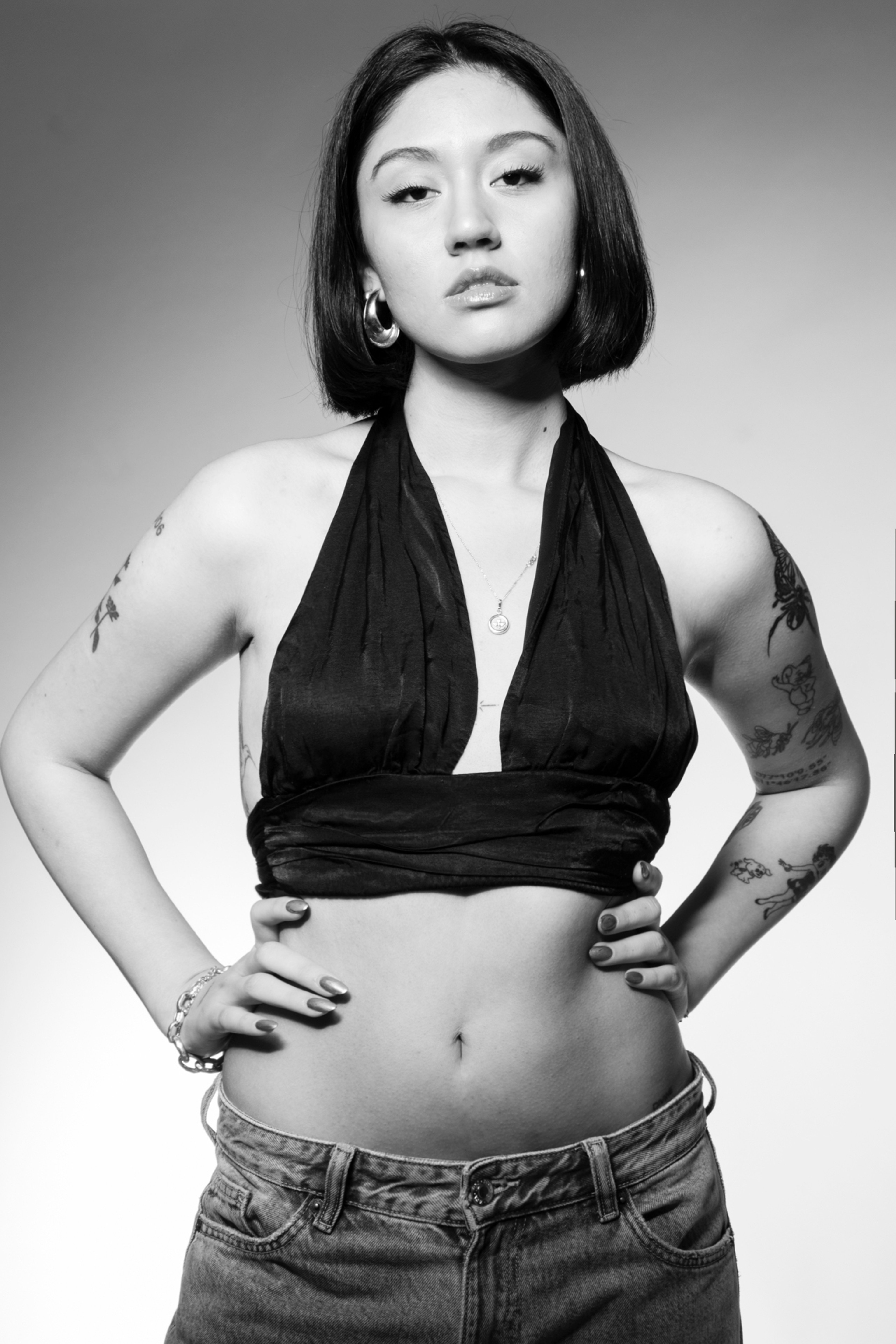 Retrato en estudio en blanco y negro de una modelo con top negro y tatuajes visibles