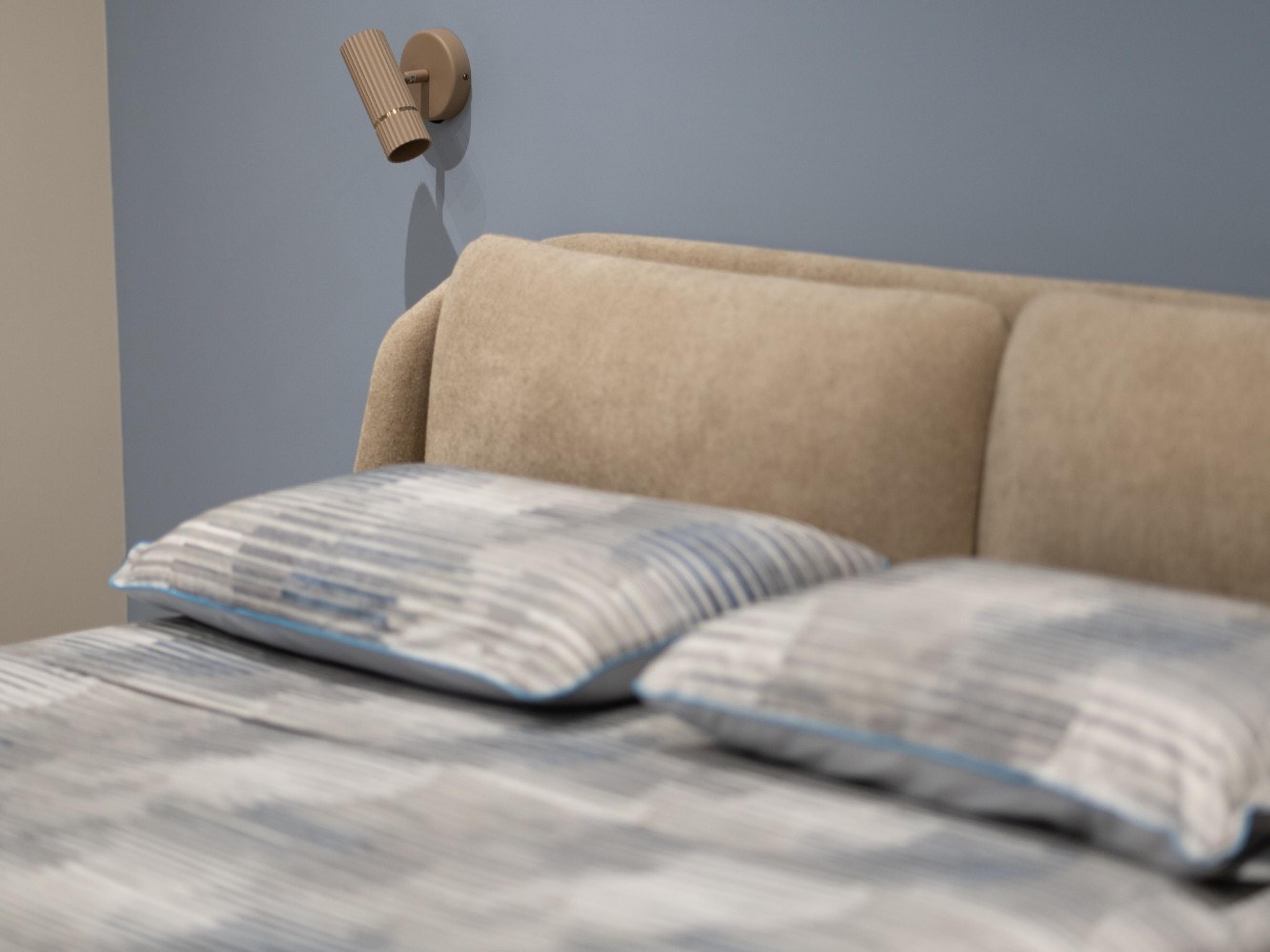 Una camera ristrutturata: letto con testata beige, cuscini a righe azzurre e una piccola lampada a parete su una parete blu