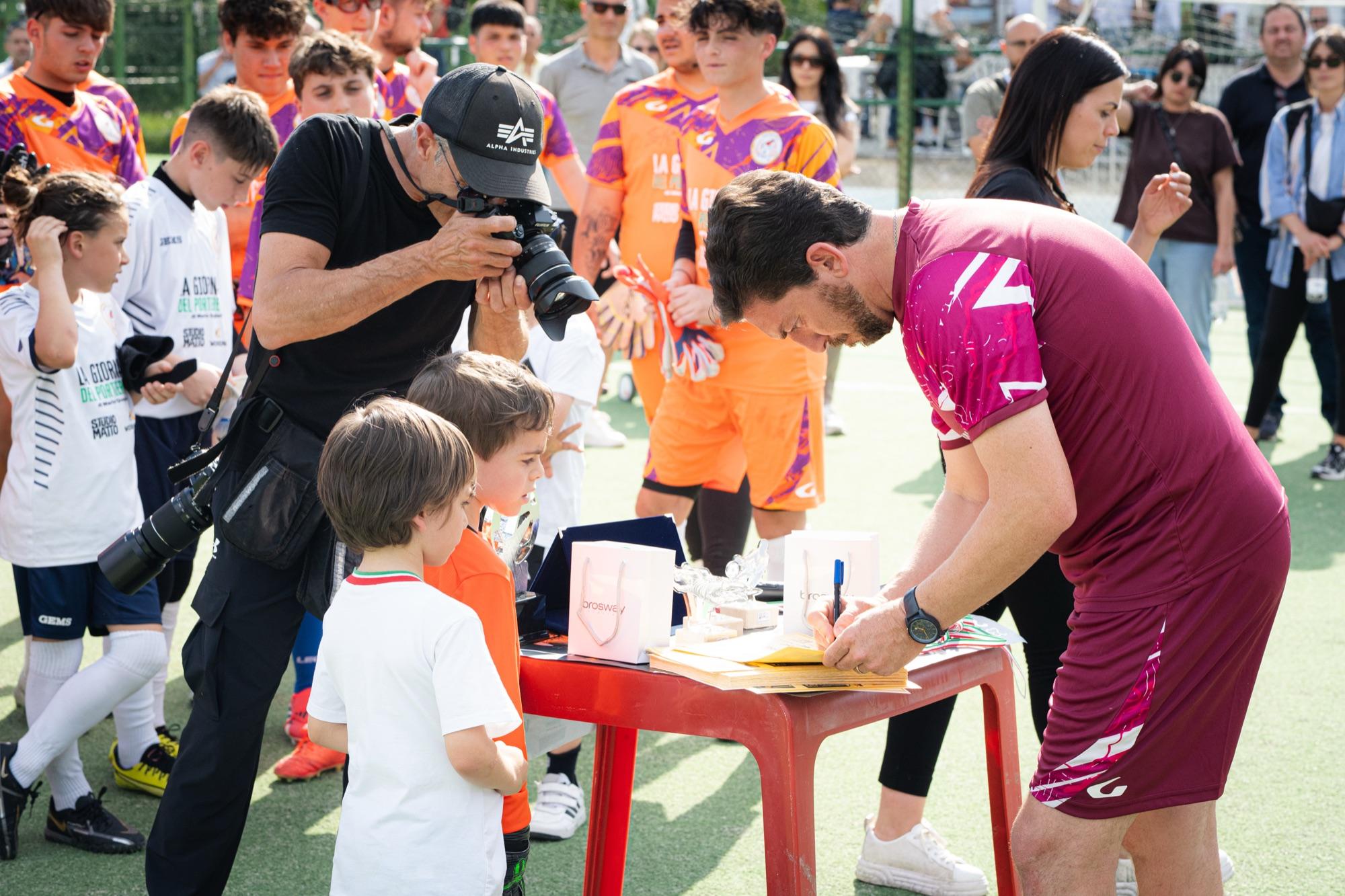 Un preparatore firma un autografo a un bambino, un fotografo scatta accanto a lui