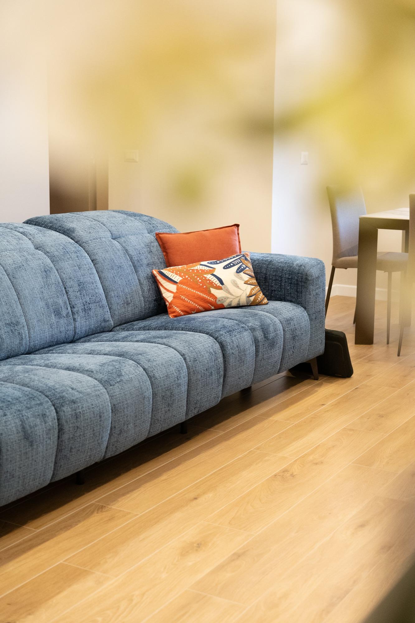 Un divano blu in un soggiorno ristrutturato, con parquet chiaro e cuscino arancione