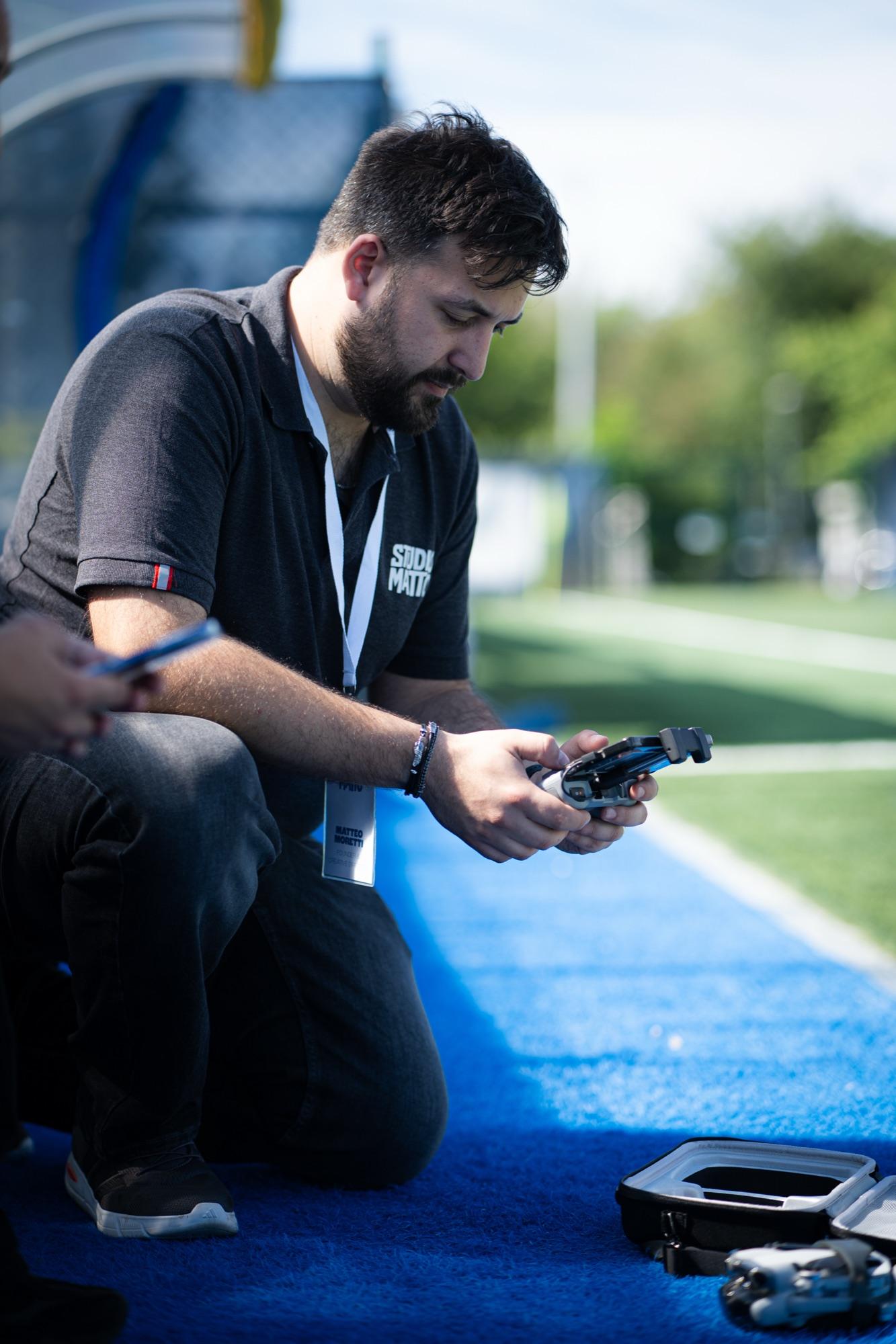 Un membro del team Studio Matto inginocchiato a bordo campo con il radiocomando del drone