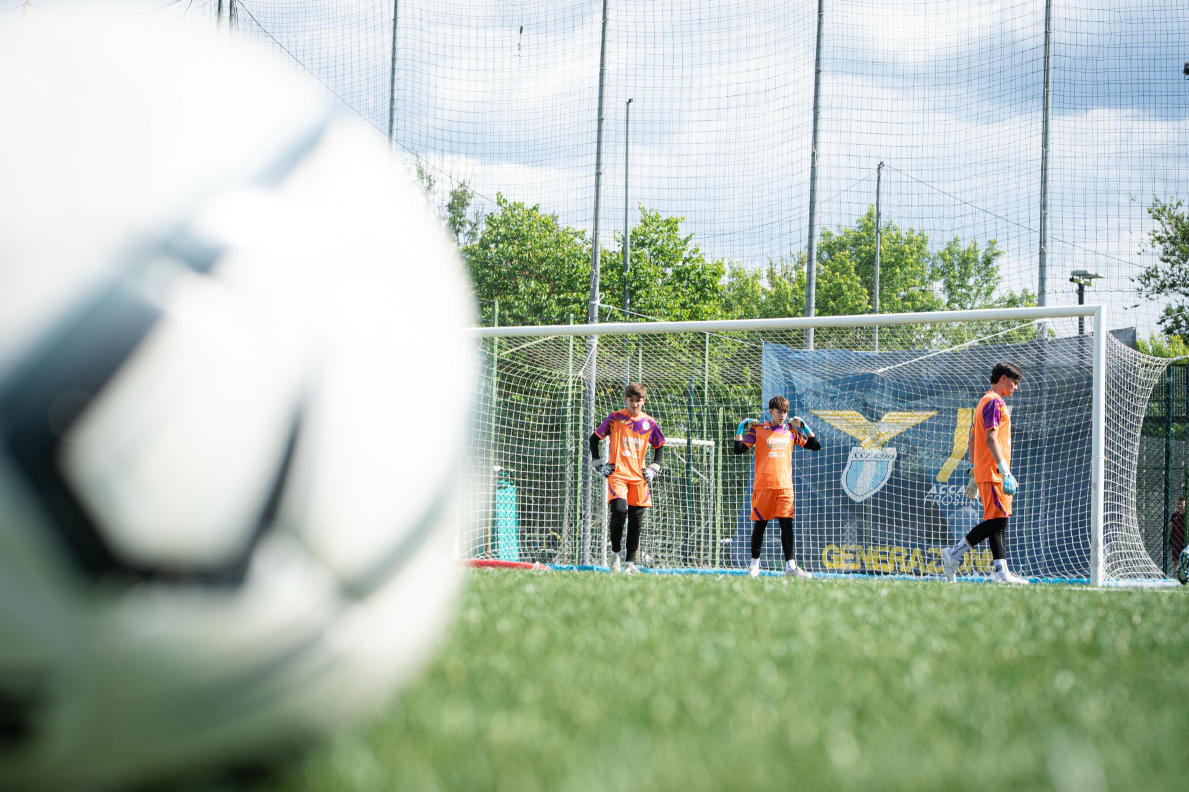 Un pallone in primo piano, dietro la porta e i portieri sfocati