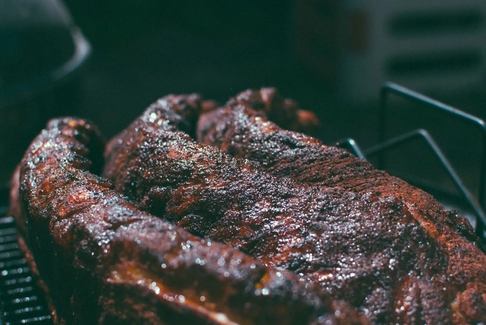 Barbecue with a dark, glistening bark resting on a smoker rack.