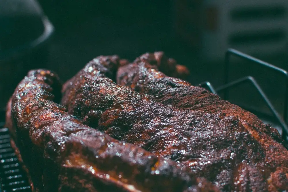 Barbecue with a dark, glistening bark resting on a smoker rack.