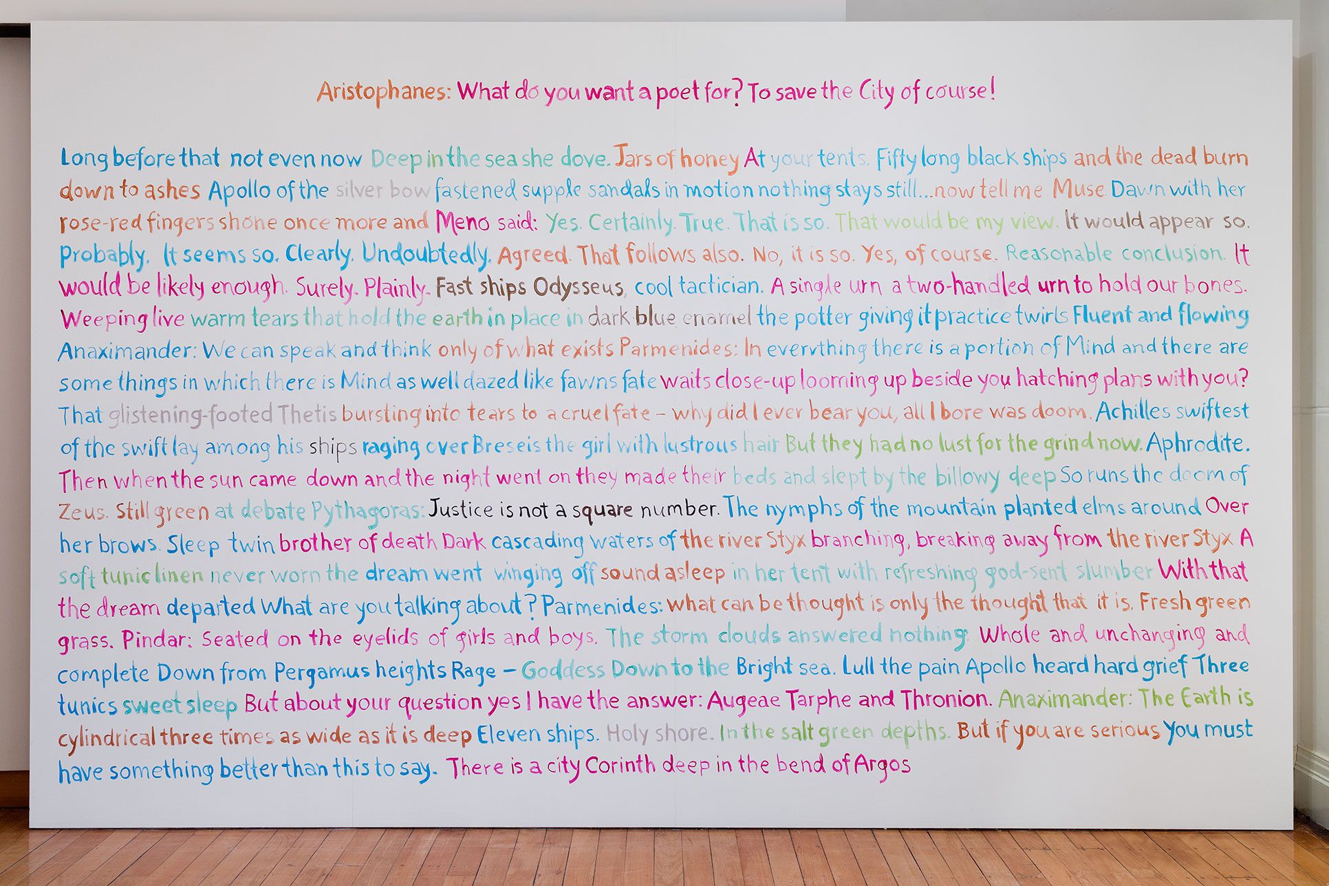 A photograph of a wall completely filled floor to ceiling with handwritten text in light blue, red and orange