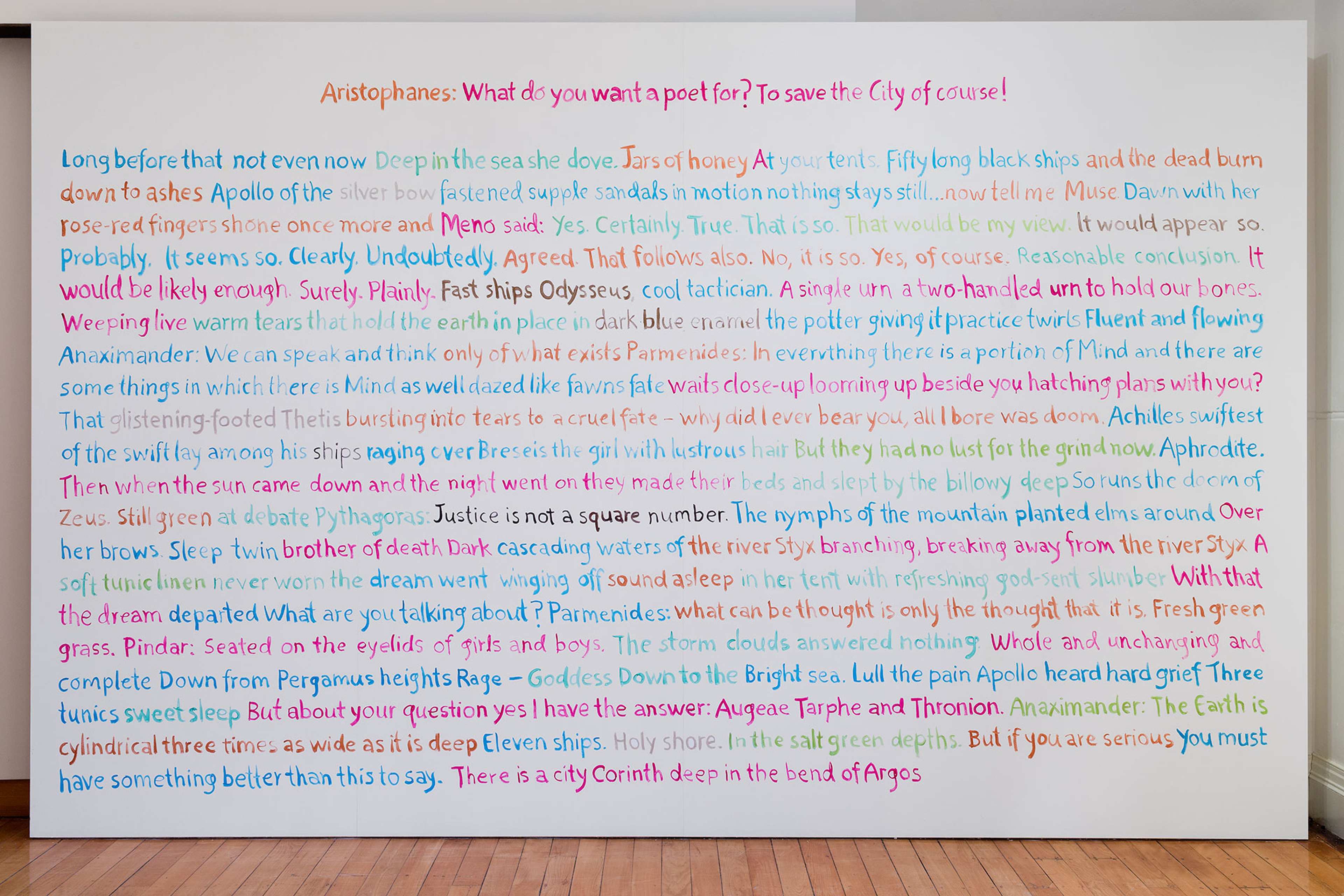 A photograph of a wall completely filled floor to ceiling with handwritten text in light blue, red and orange