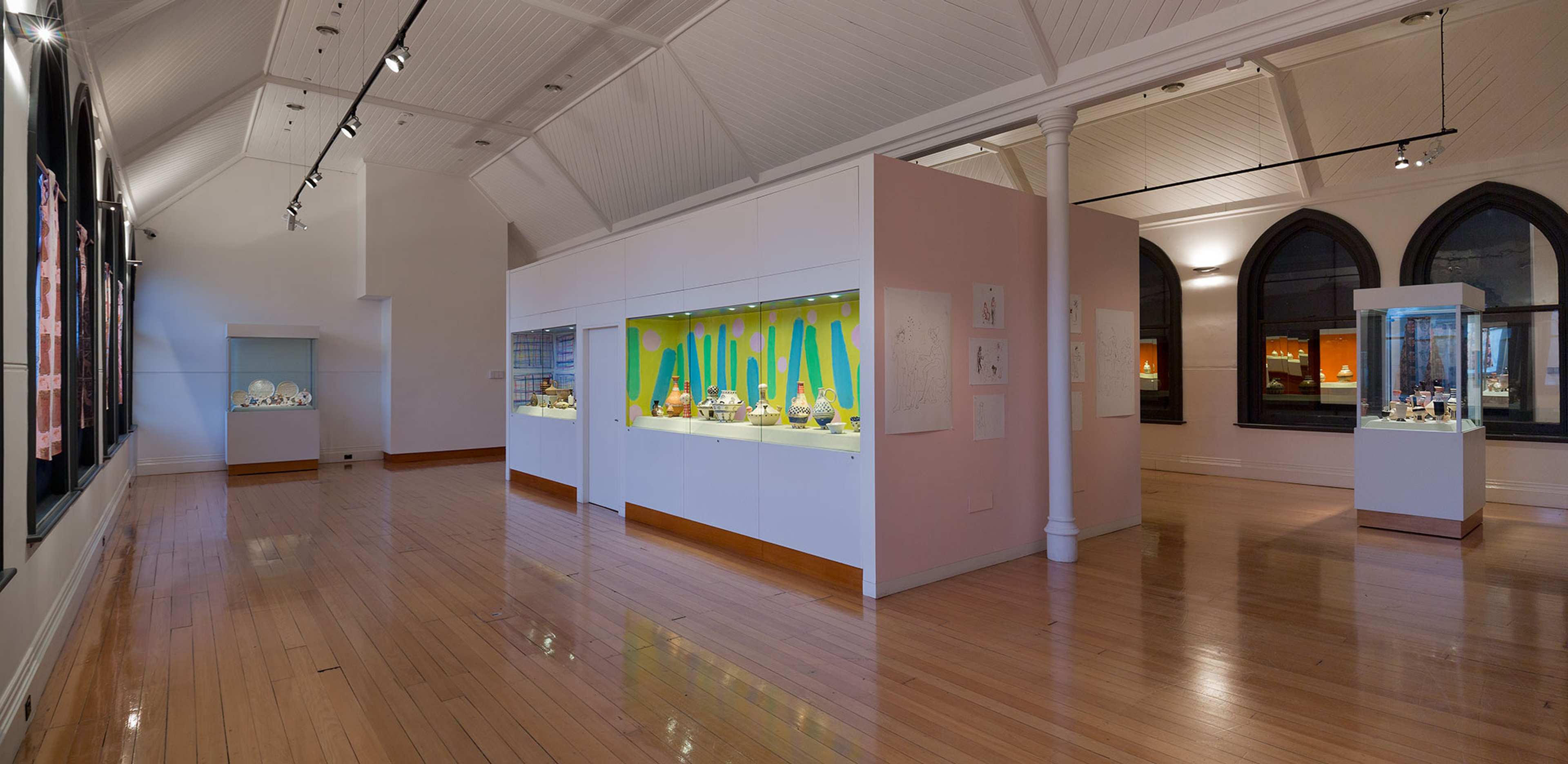 A wide shot of gallery space with multiple vitrines with colourful objects