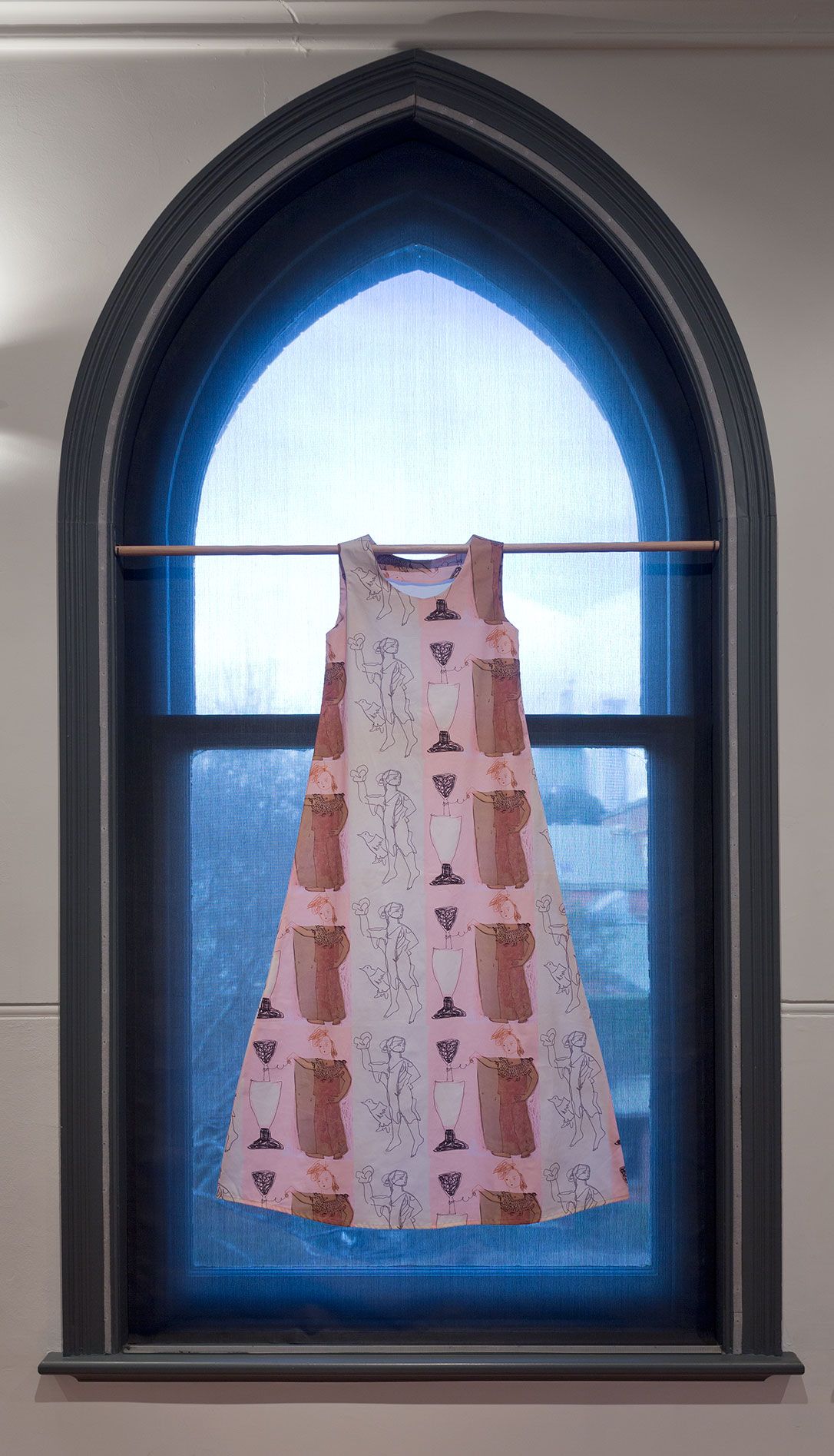 A photograph of a simple dress with a repeating graphic pattern hanging from a rod in an arched window