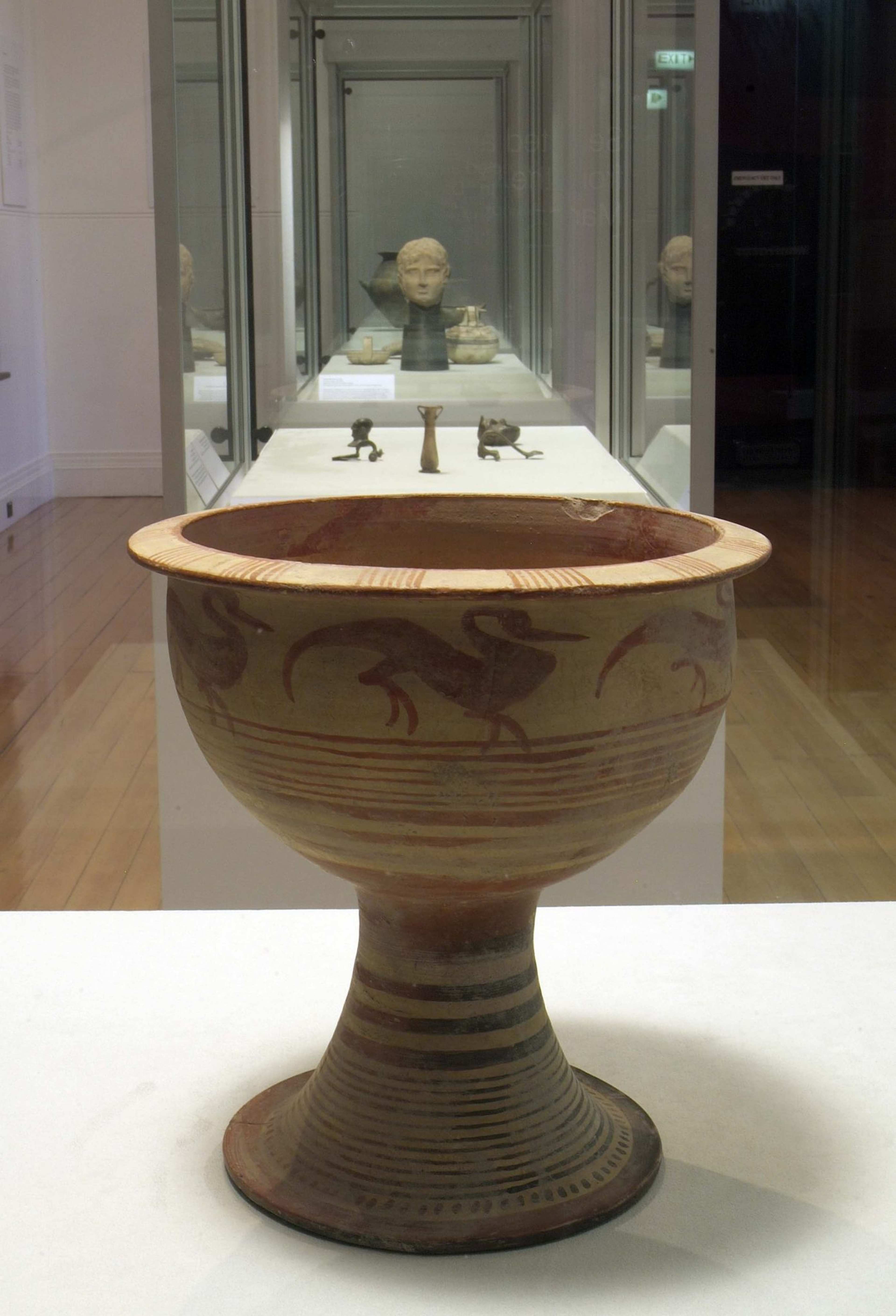 A photograph of a gallery space with an ancient clay vessel in the foreground
