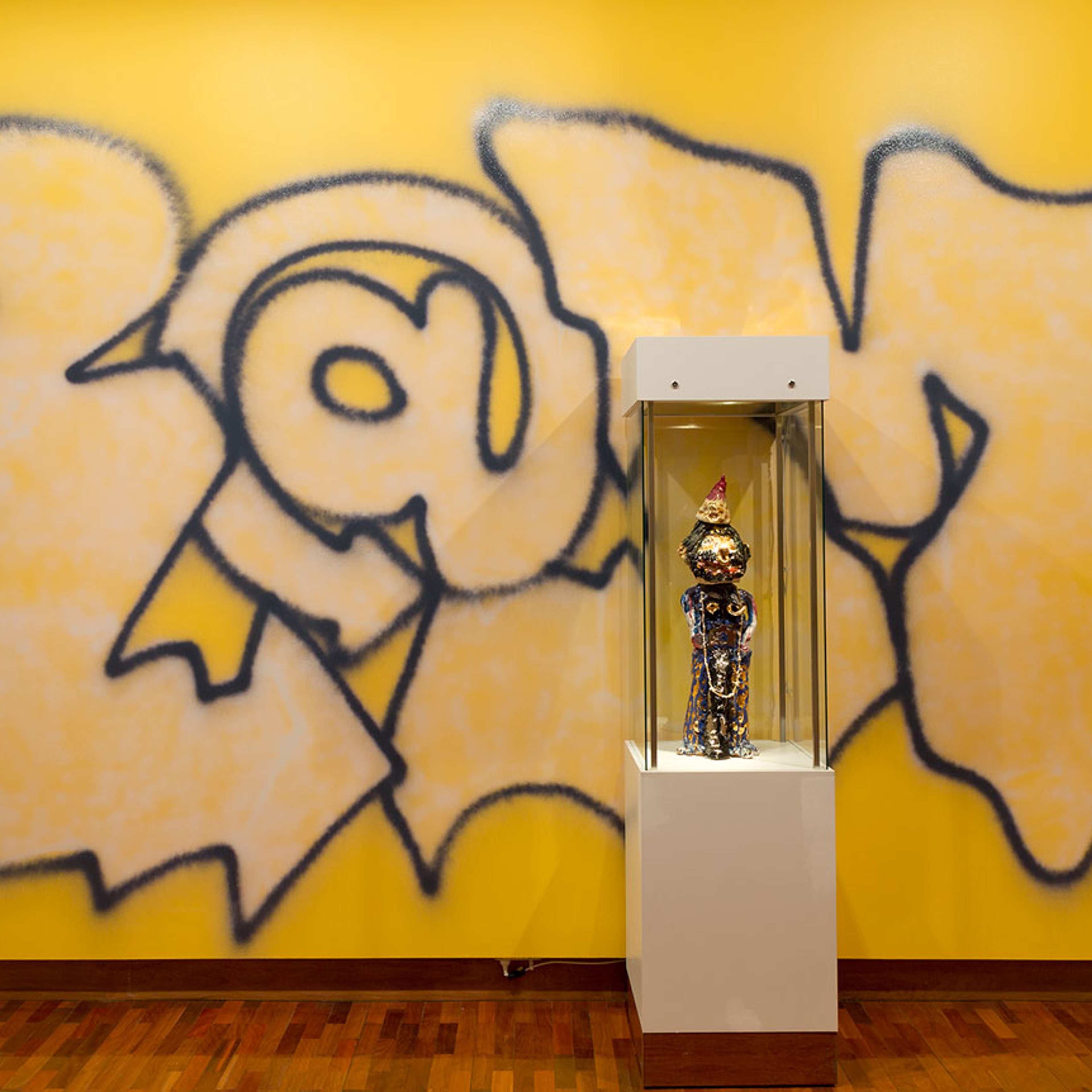 Grafitti style art on of the artists name a yellow wall with a sculpture on a plinth