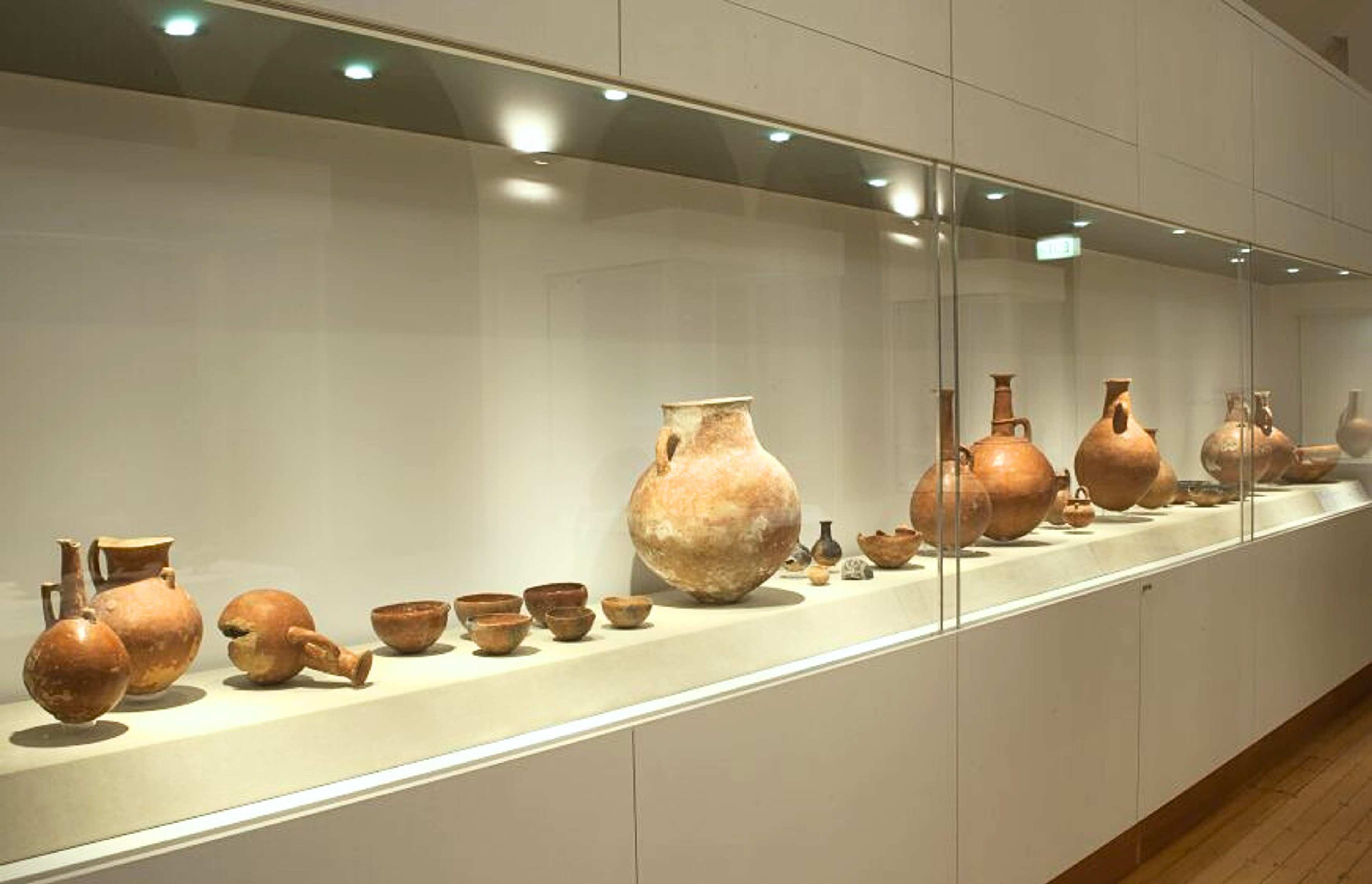 A photograph of a longe vitrine with a row of variously shaped terracotta vessels in it