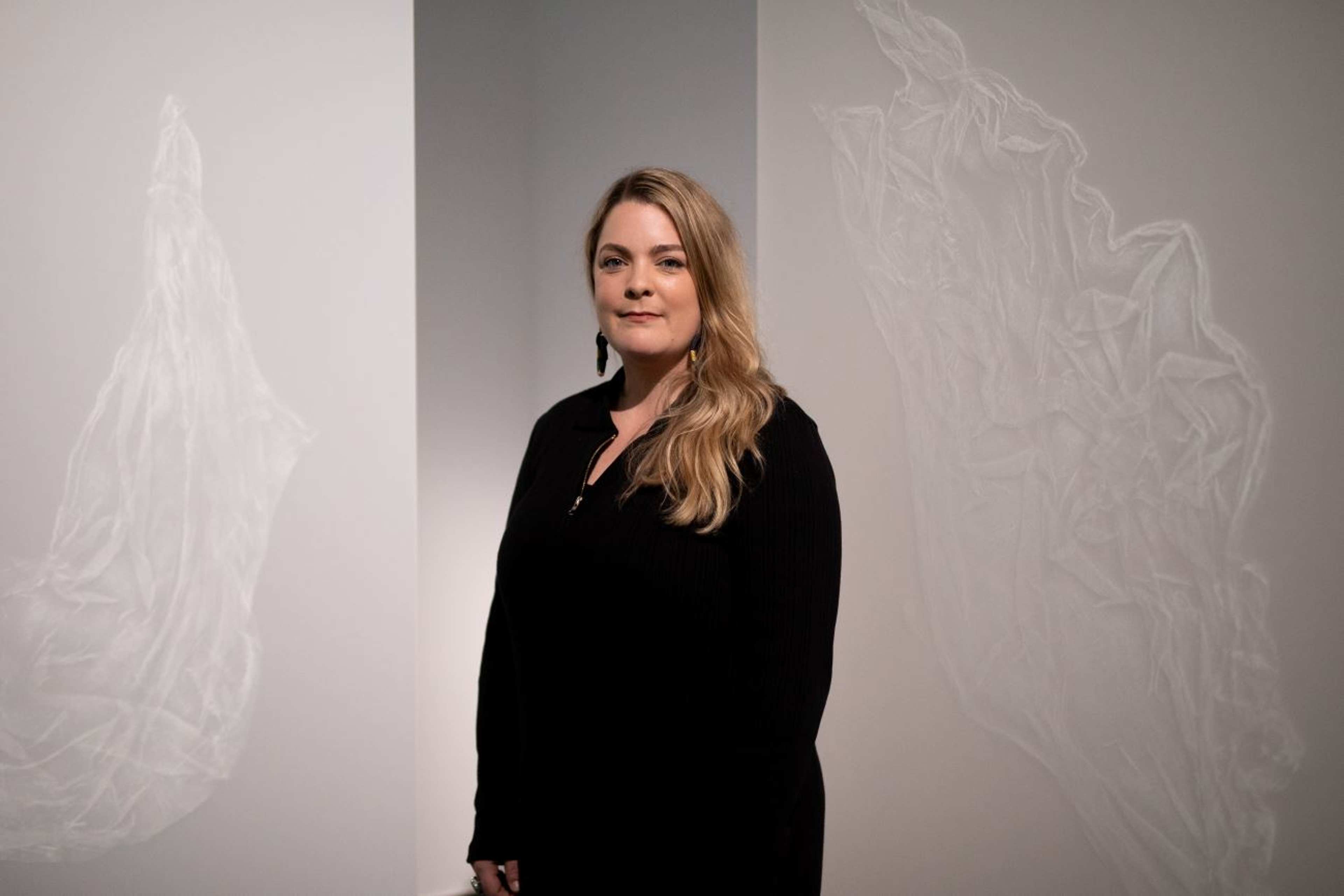 A person in a black stands in front of her artwork a white pattern on beige paper