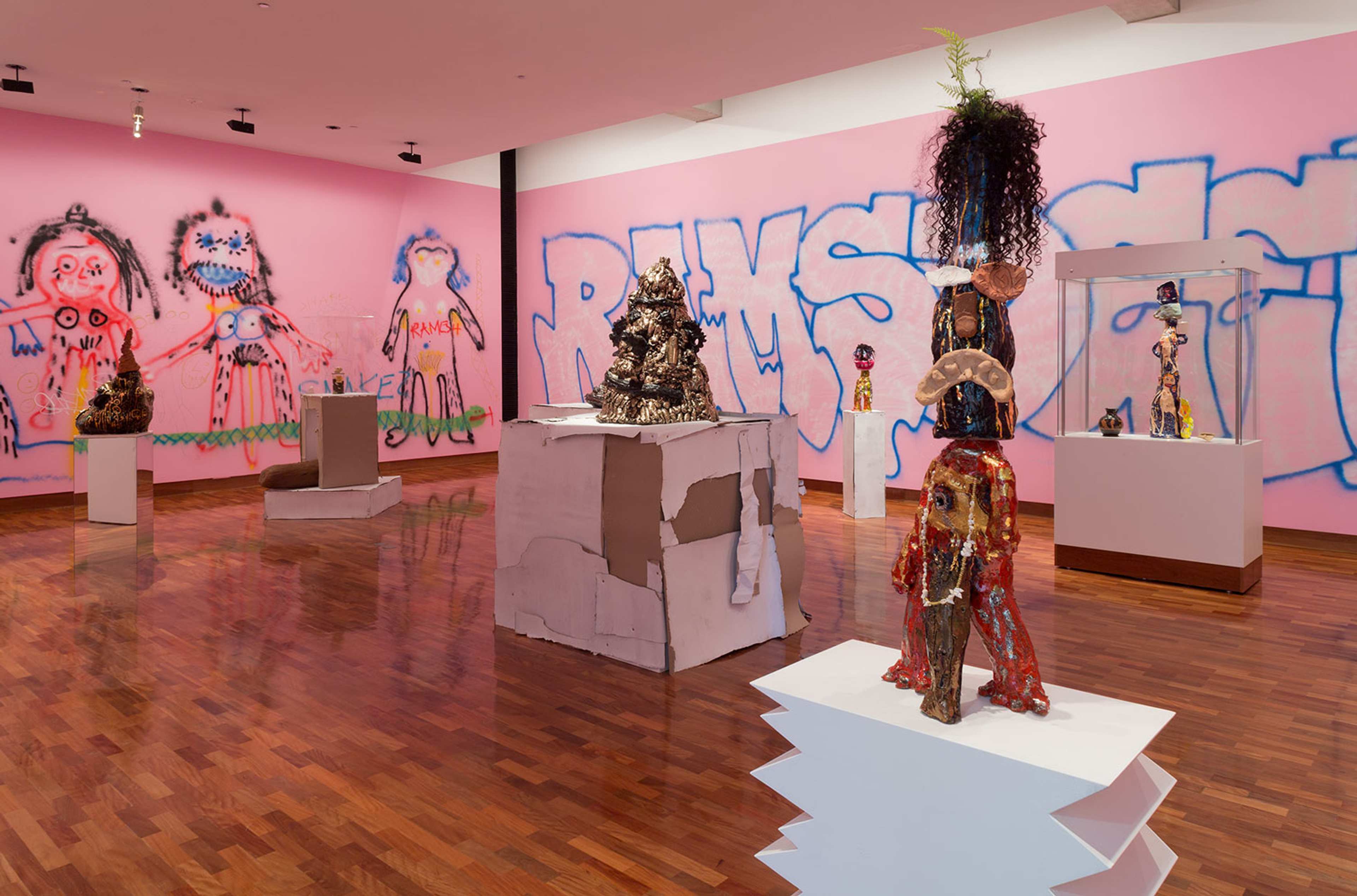 A wide shot of a pink gallery space with sculptures on plinthes
