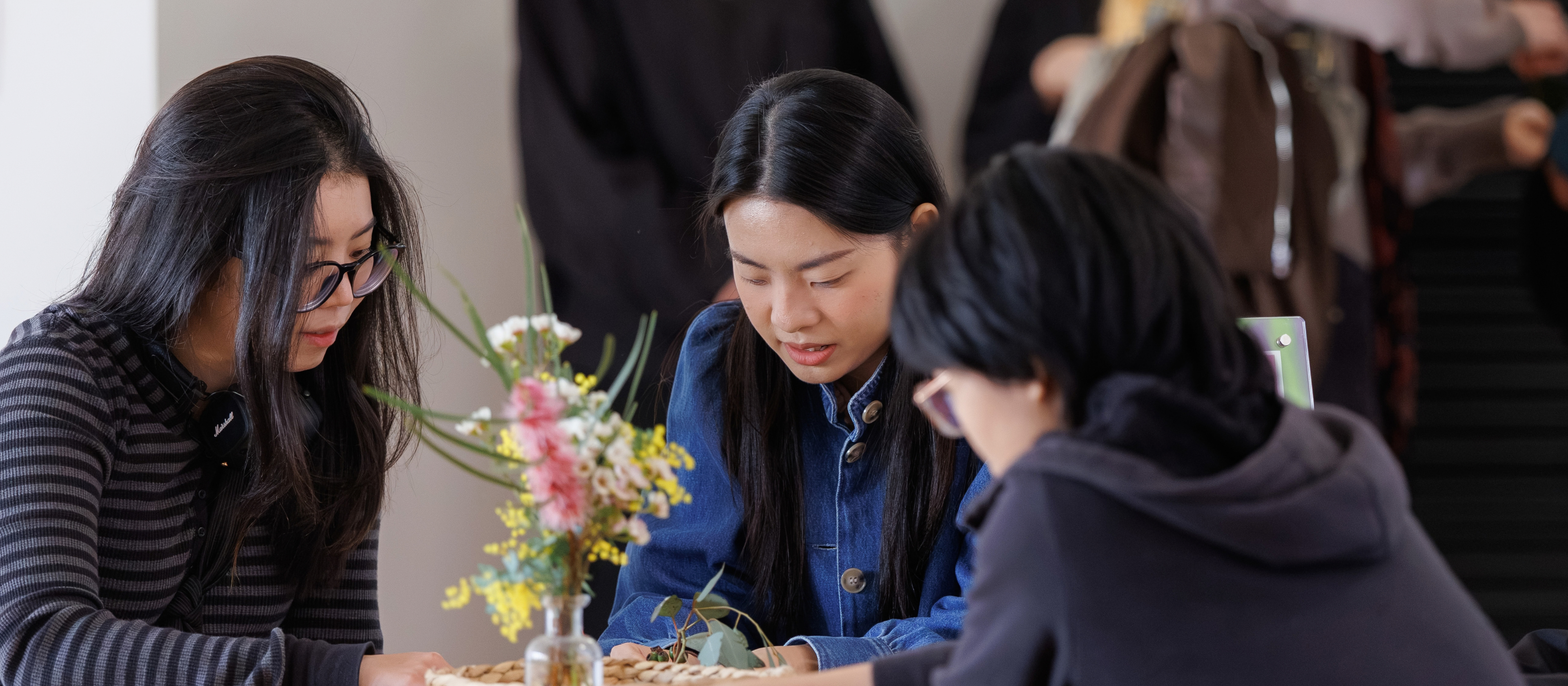 Three young adults, sitting on a table looking down at natural materials on a table.