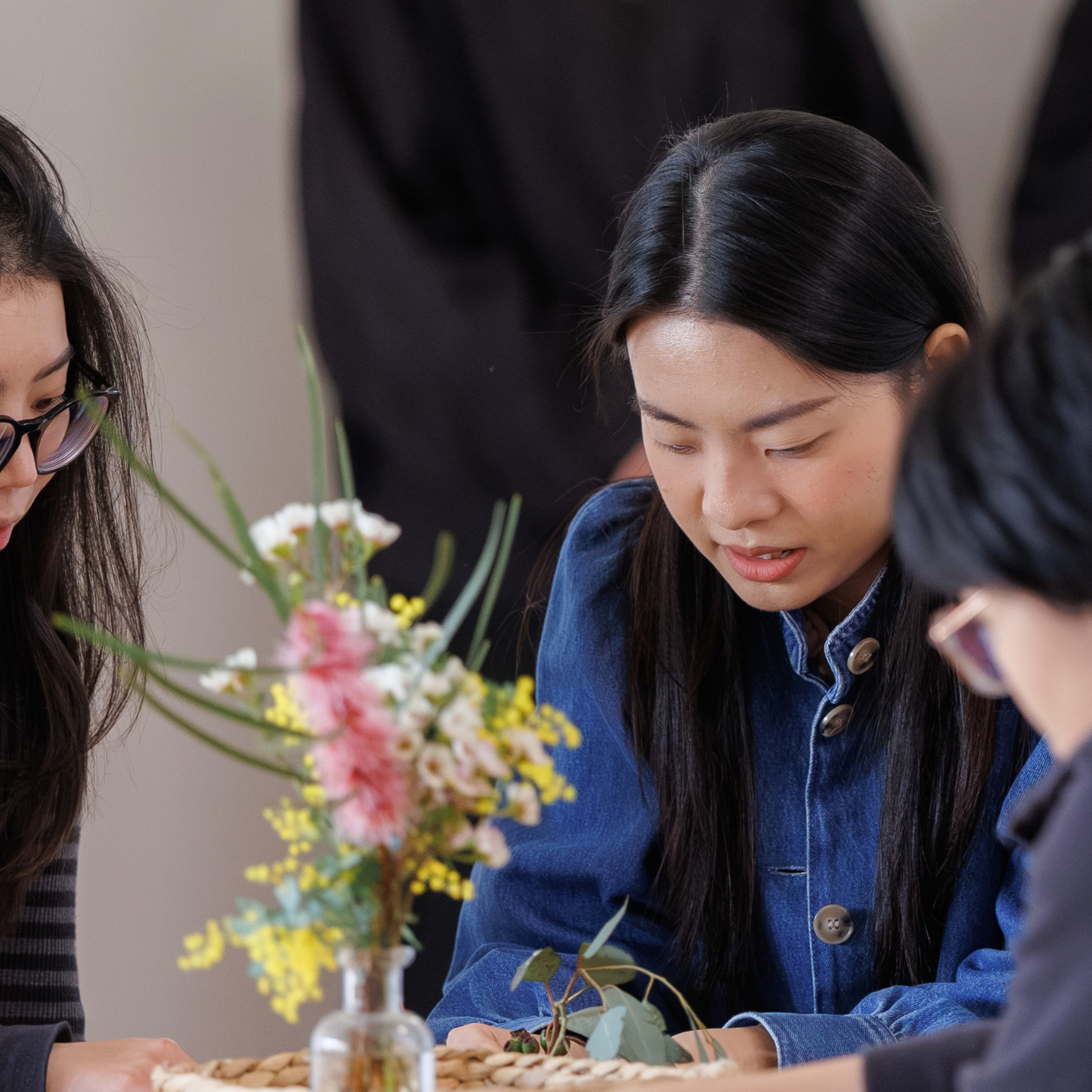Three young adults, sitting on a table looking down at natural materials on a table.