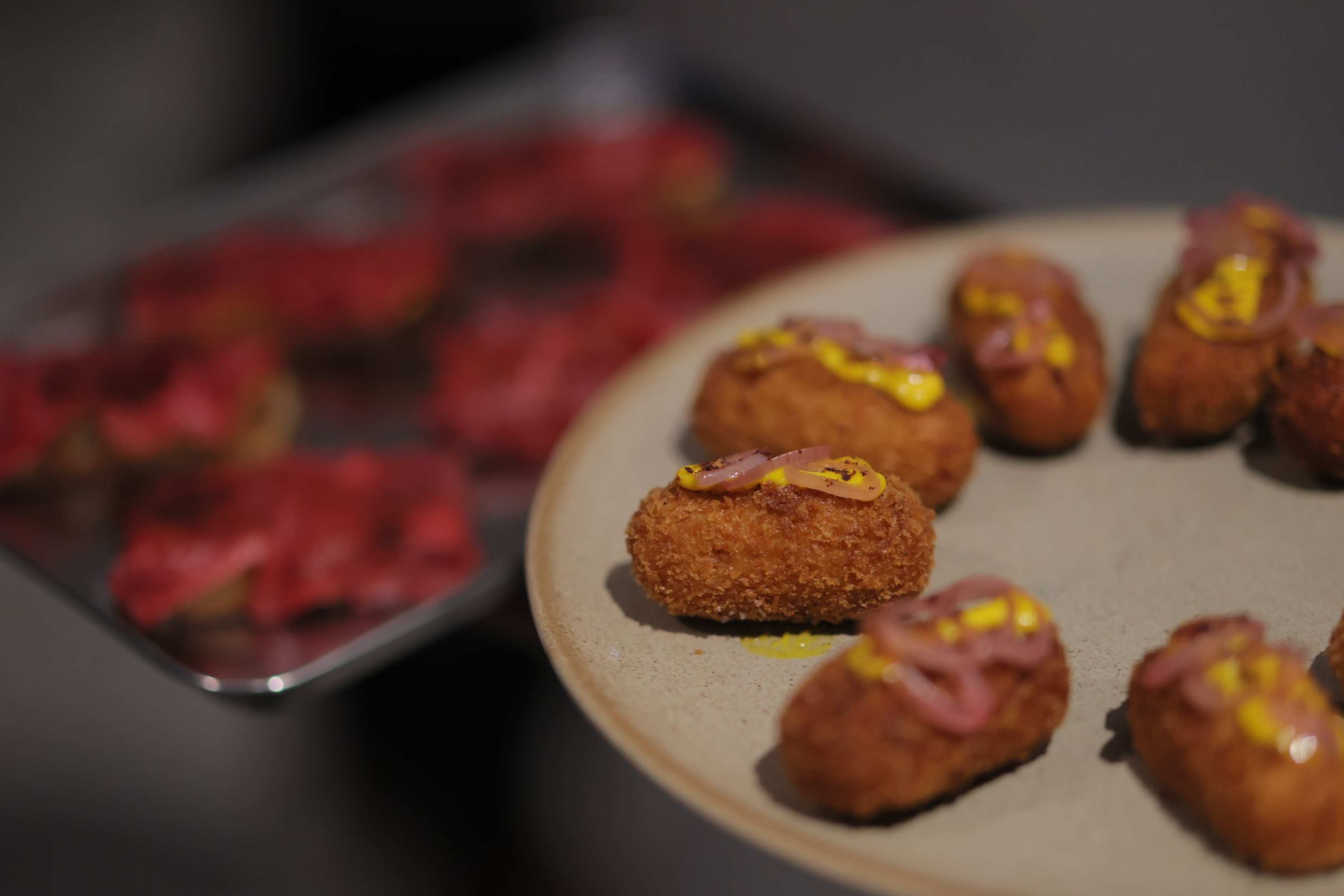 Croquettes with a yellow sauce are lined on a grey plate.