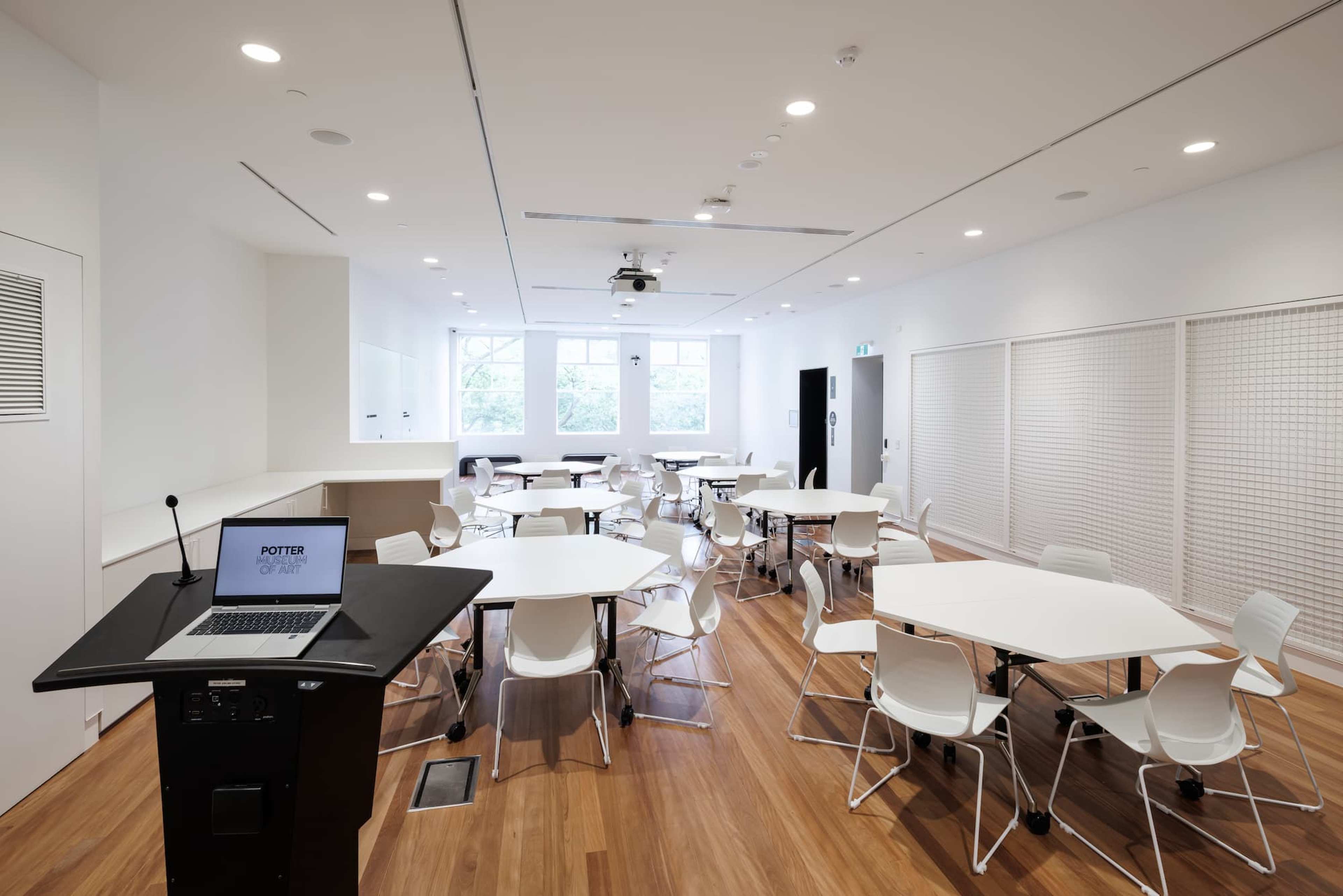 A white room with 6 round white tables and chairs and a lectern with a computer in the front